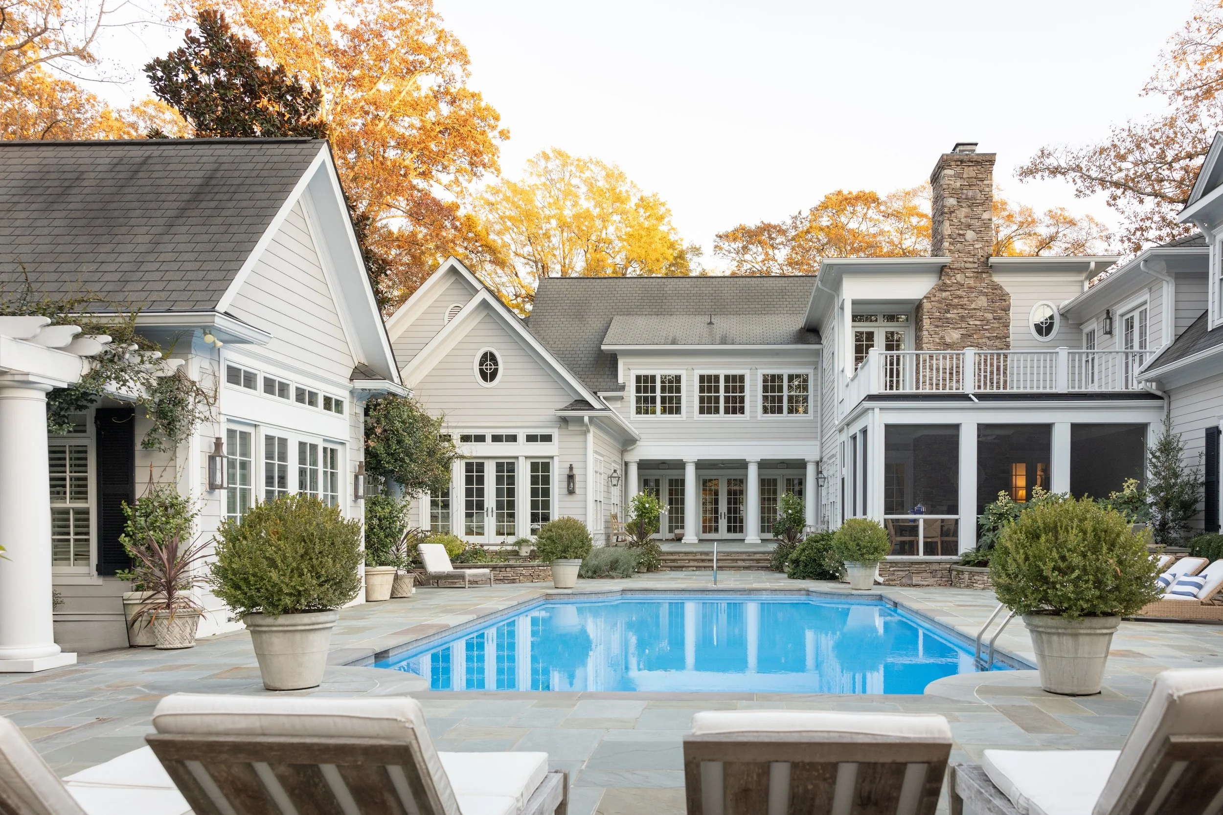 Luxury custom home in the Triangle NC with a backyard pool, covered outdoor living space, stone chimney, and upscale exterior design by a custom home builder