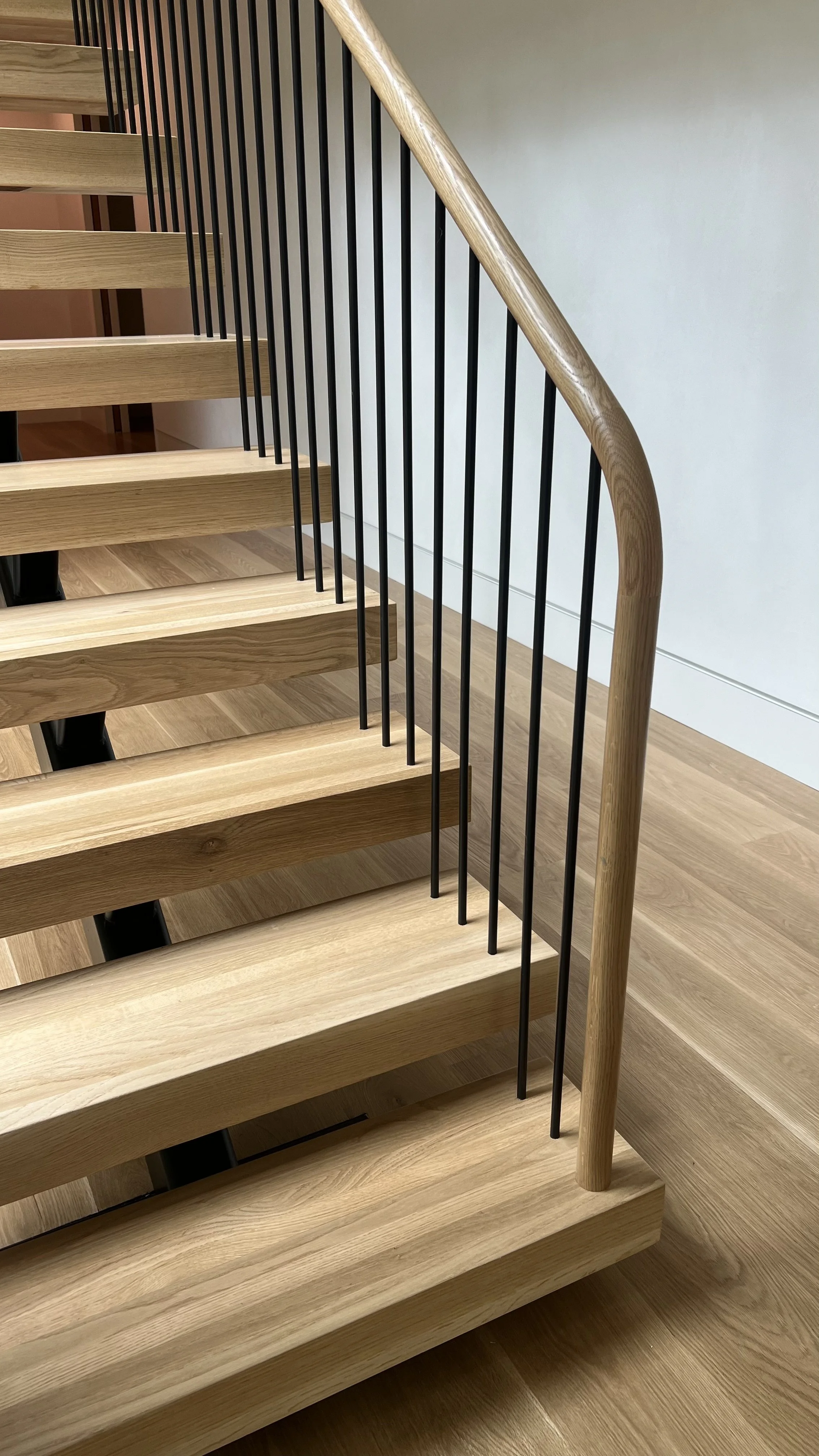 Close-up of a modern wooden staircase with black metal balusters and a curved wooden handrail.