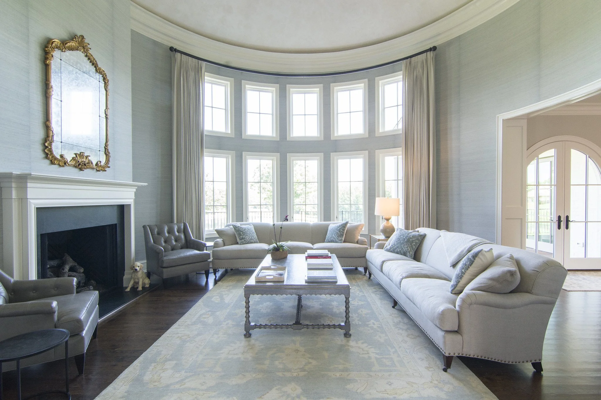 Living room interior of a luxury custom home by Will Johnson Building Company in the Triangle NC featuring tall windows, curved wall, fireplace, and bright open residential design