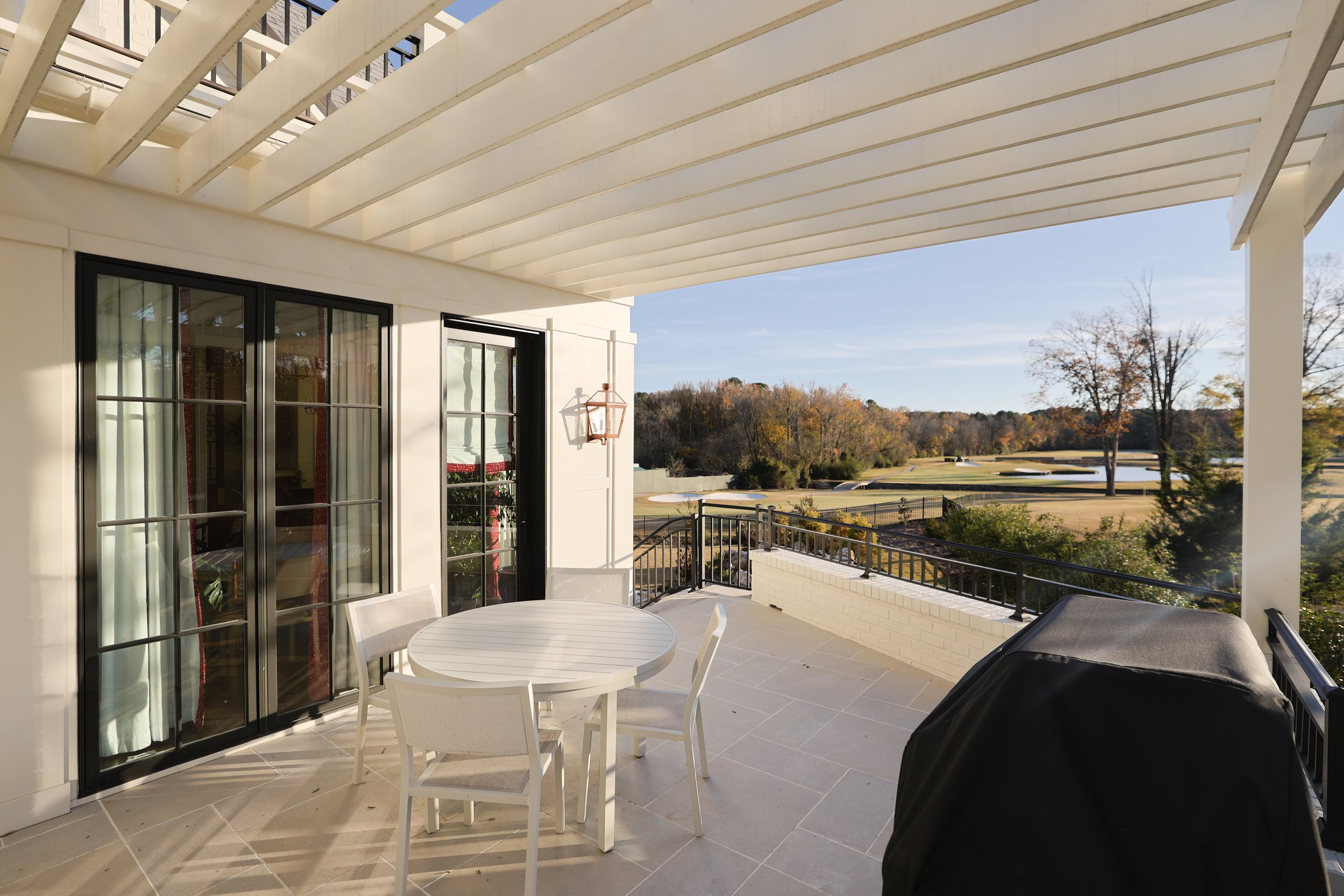 A spacious balcony with a white round table and four white chairs, overlooking a golf course with trees and a clear sky.
