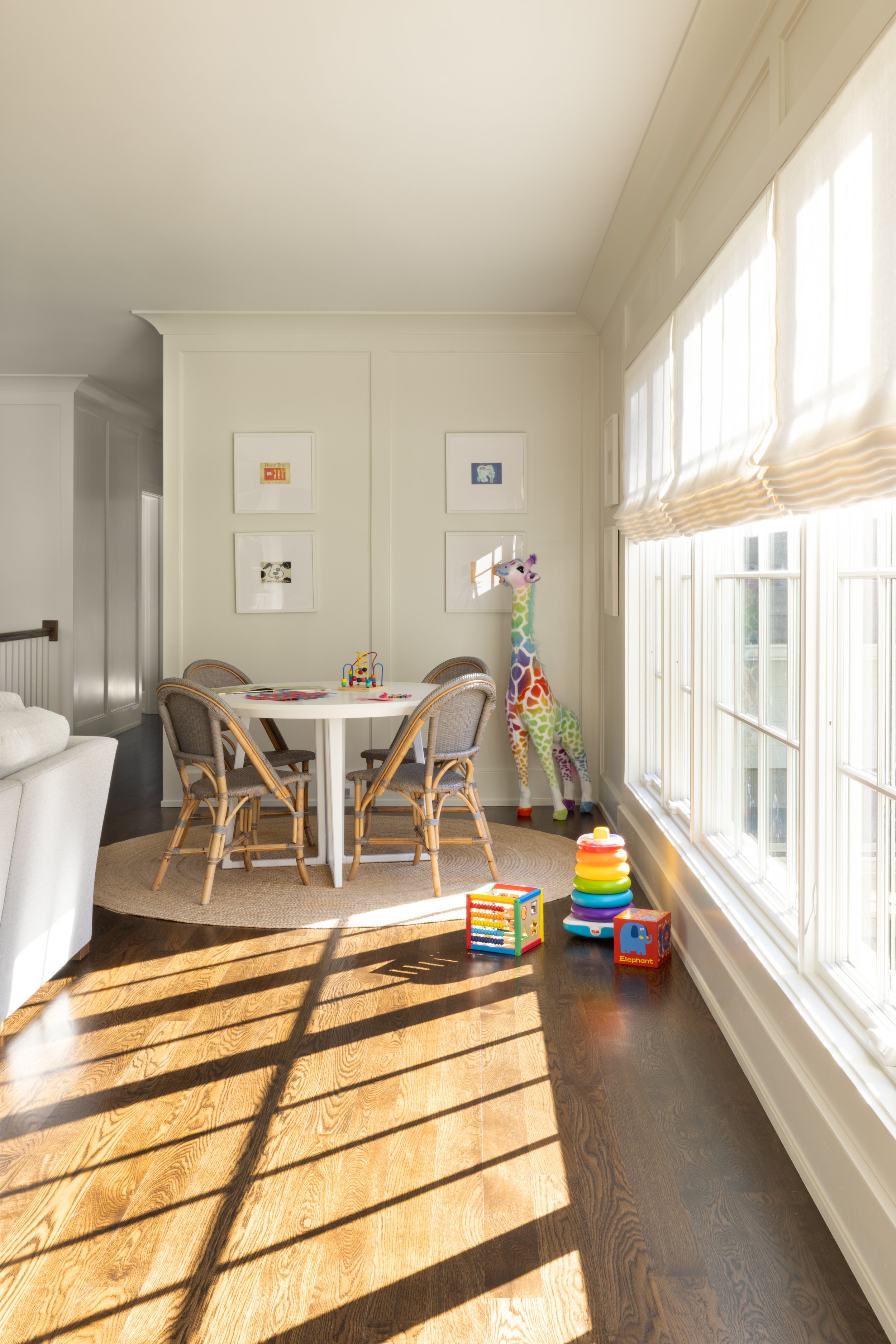 Sunlit children's playroom with toys, a rainbow giraffe plush, and framed artwork.