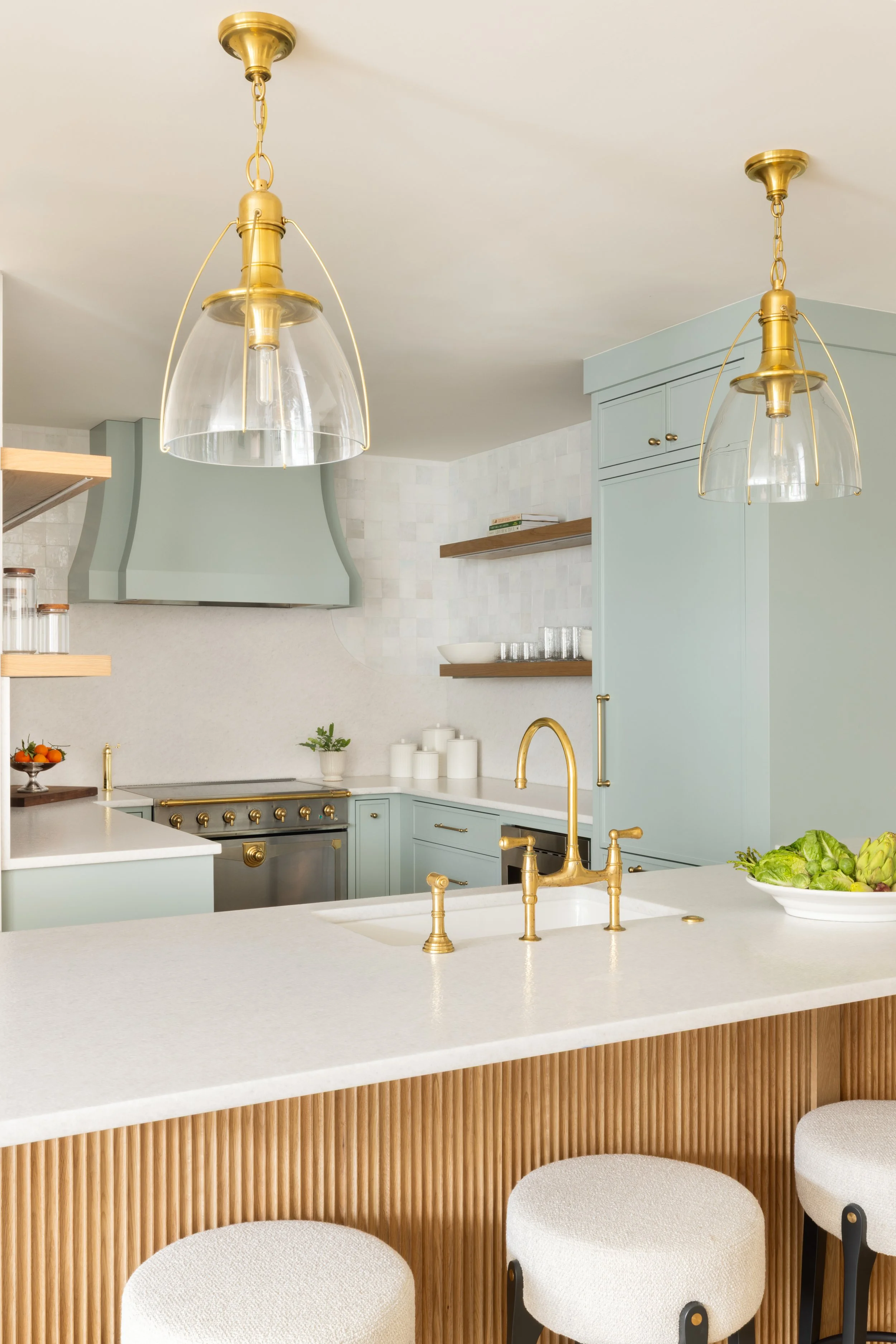 Modern kitchen with pastel blue cabinetry, gold fixtures, white countertops, open shelving, and a neutral color palette.