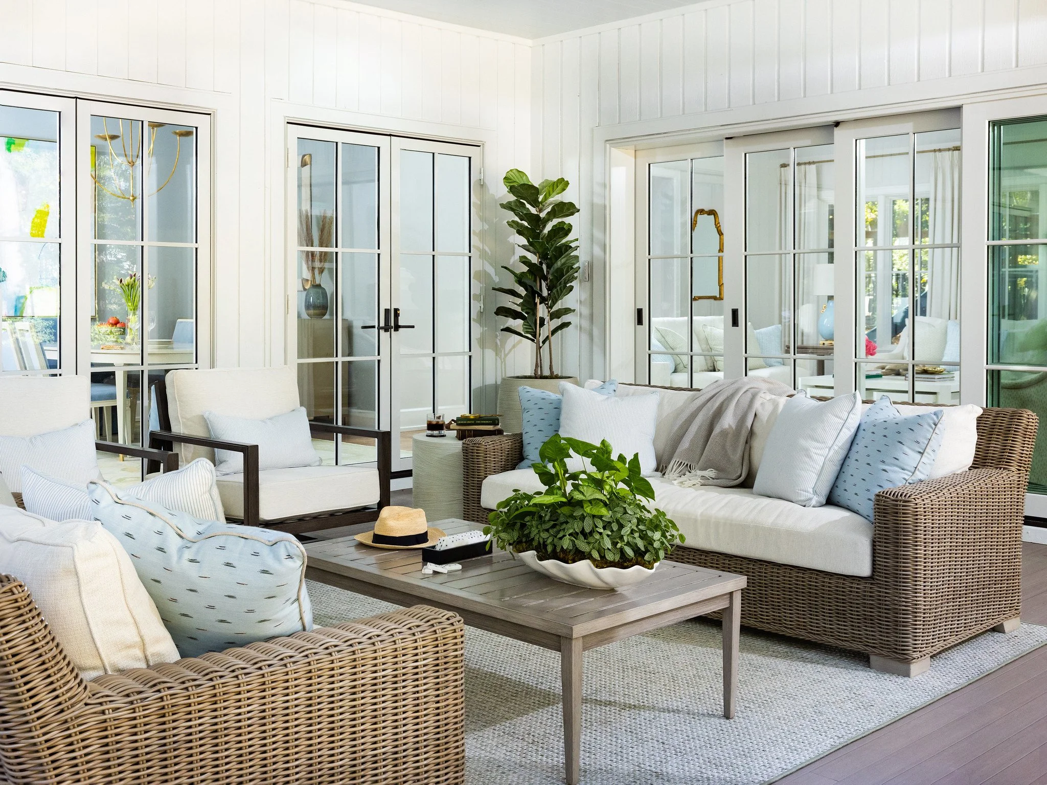 Bright sunroom with wicker and upholstered seating, glass sliding doors, and green plants.