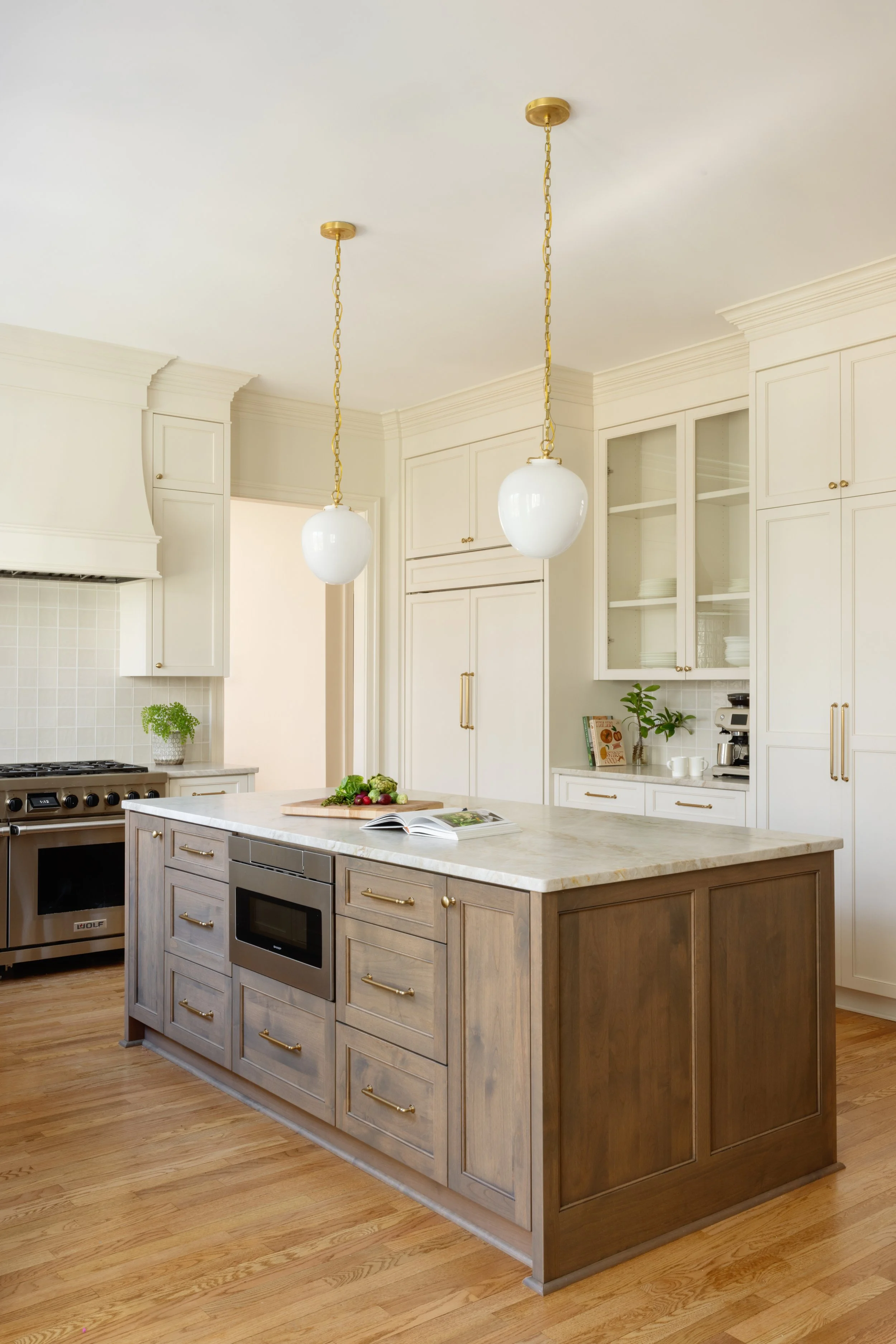 Modern kitchen with white cabinets, a central island with a marble top, two hanging pendant lights, and a hardwood floor.