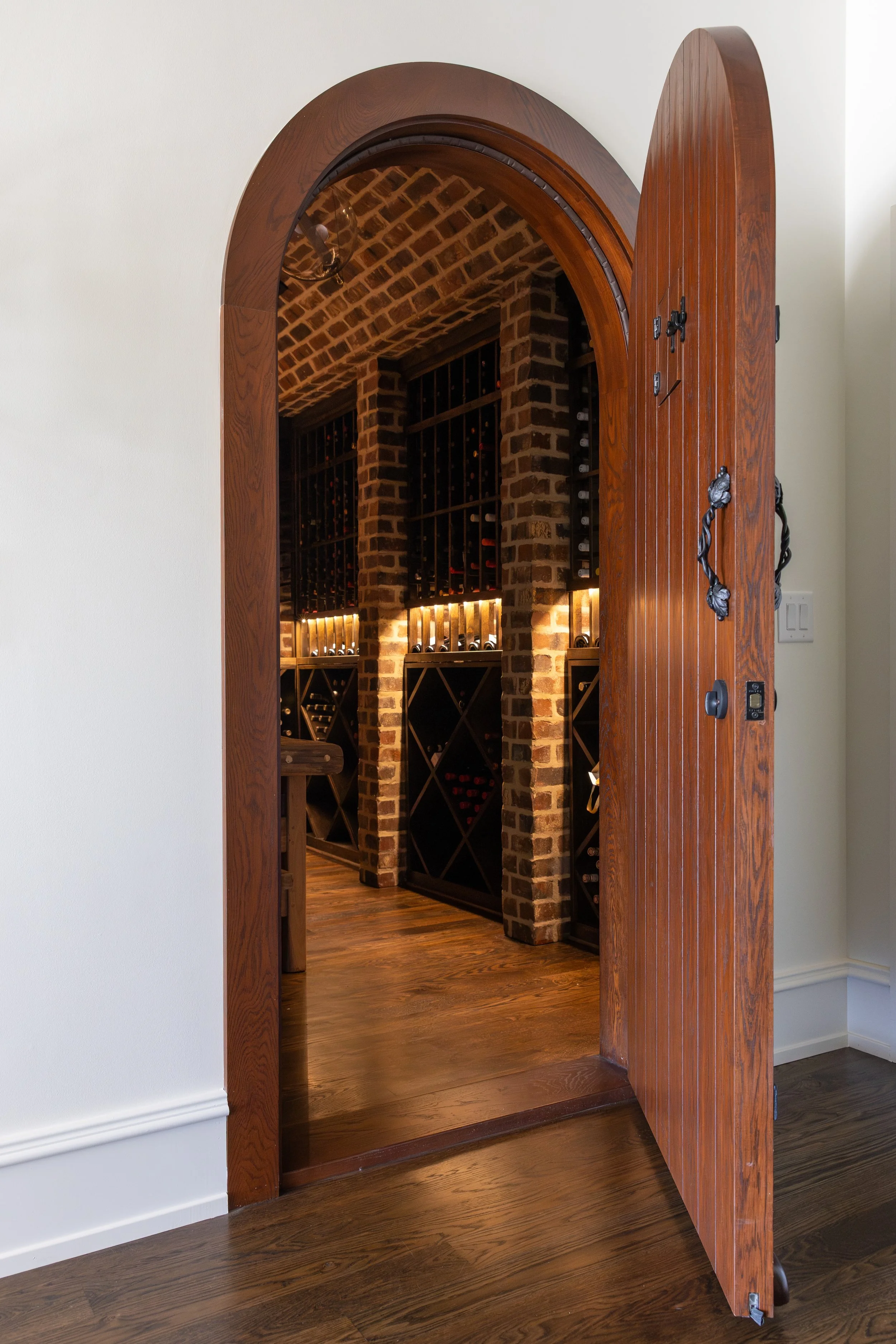 View through a wooden door into a wine cellar with brick walls and wine racks.