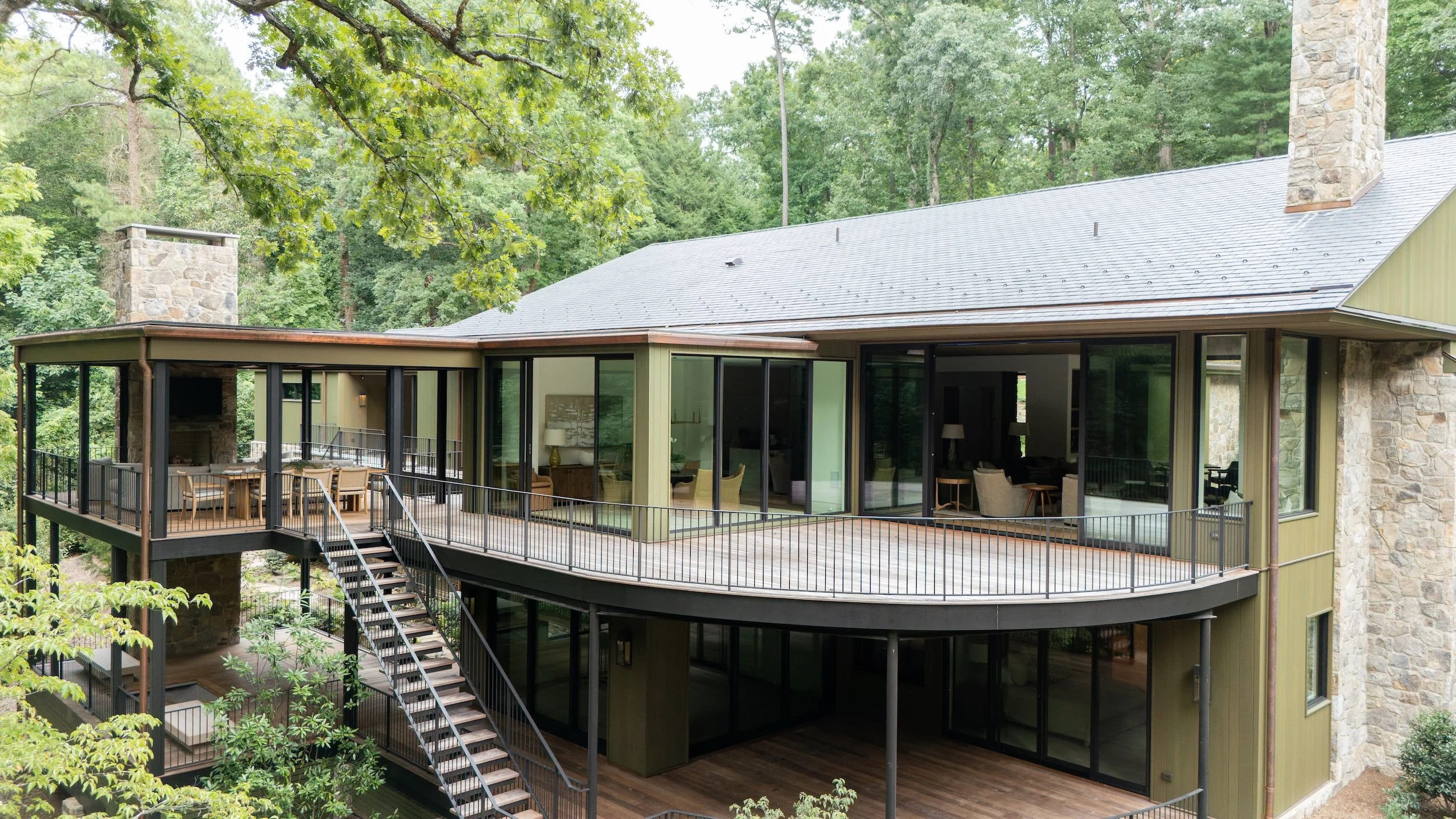Modern multi-level house with large glass windows and surrounded by trees.