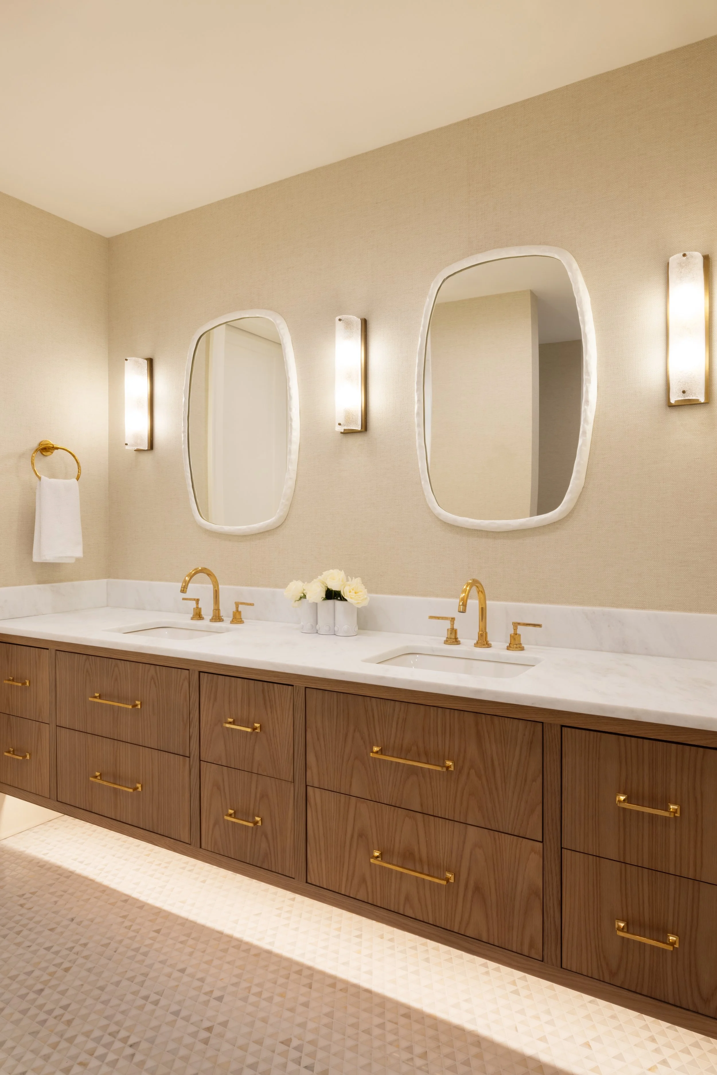 A luxurious bathroom with two mirrors, gold fixtures, a marble countertop, and a wooden vanity with gold handles.