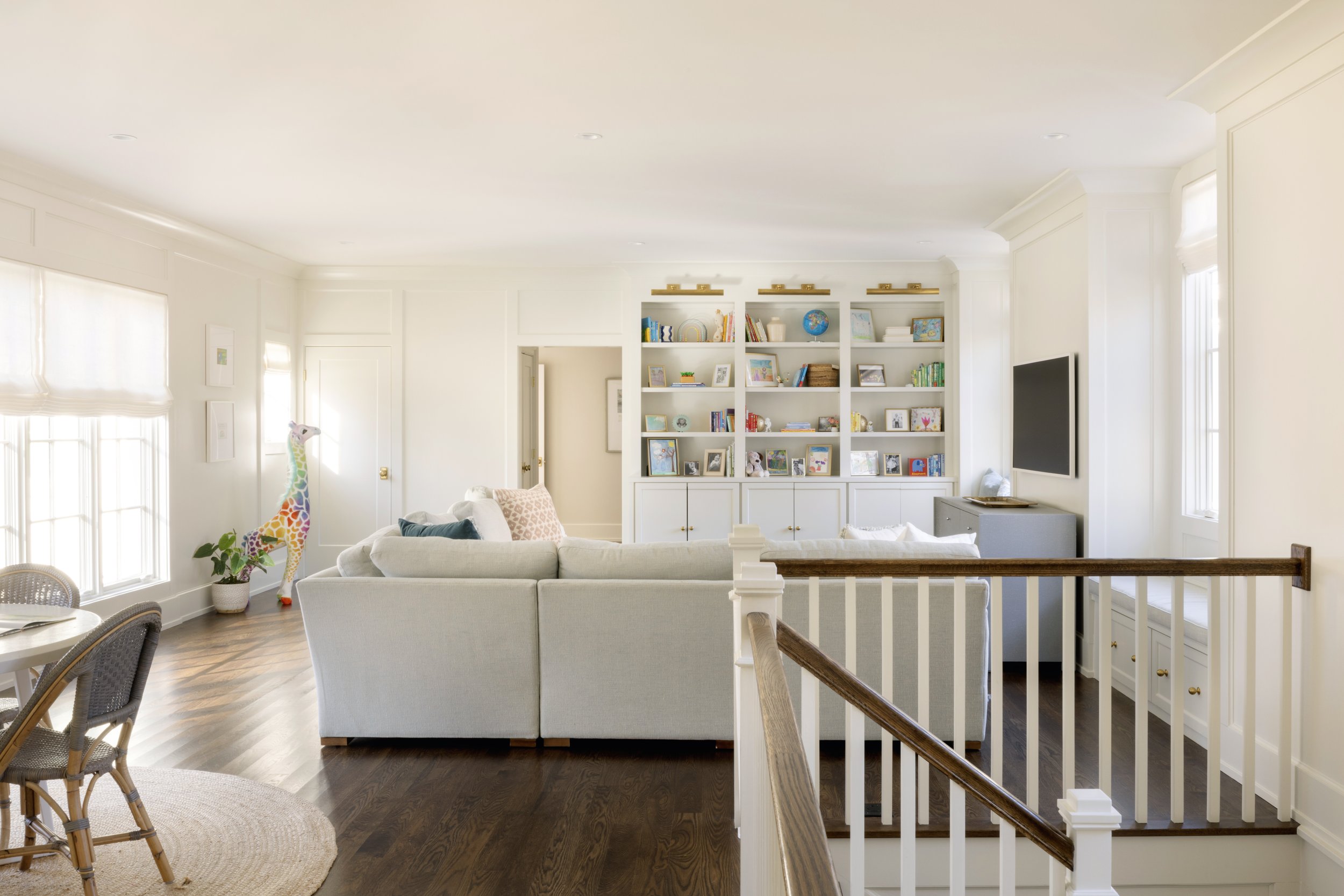Living room with white sofa, built-in bookshelves, dark hardwood floor, and large windows flooded with natural light.