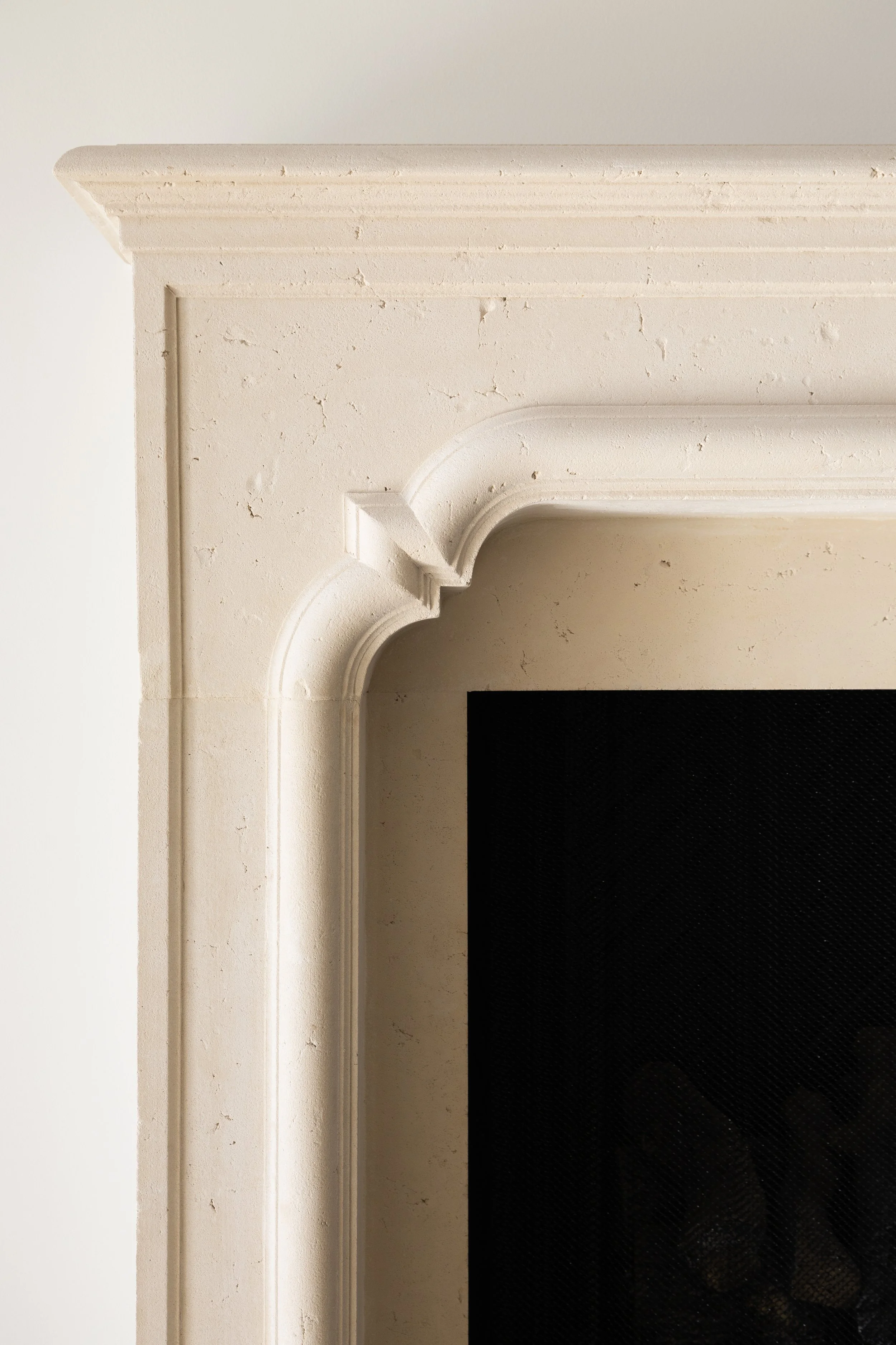 Close-up of a beige fireplace mantel with decorative molding, partially showing a black surround and white wall.