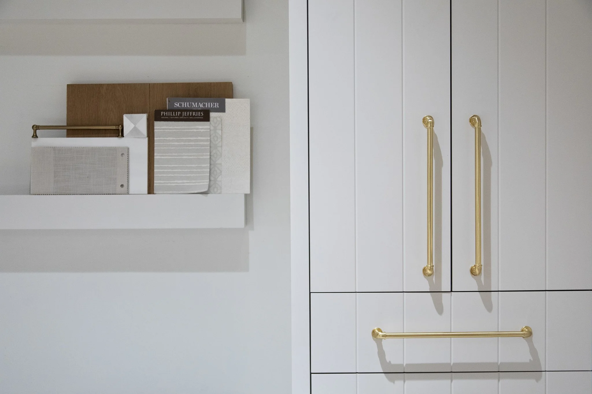 Display of fabric samples and color swatches on a white wall next to a white cabinet with gold handles.