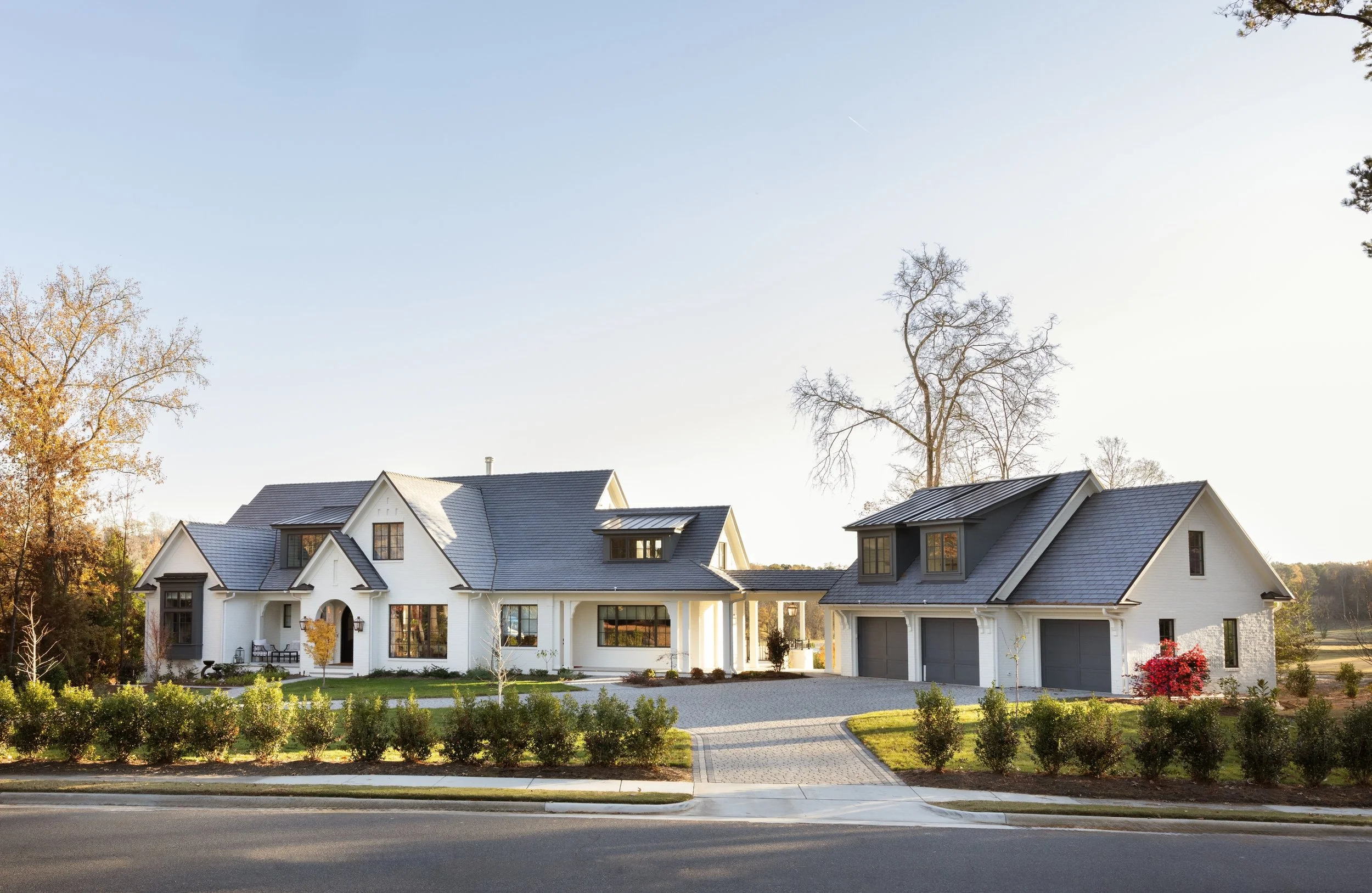Luxury custom home in the Triangle featuring white brick, black-framed windows, layered rooflines, detached garage, and landscaped grounds designed for timeless curb appeal and long-term living.