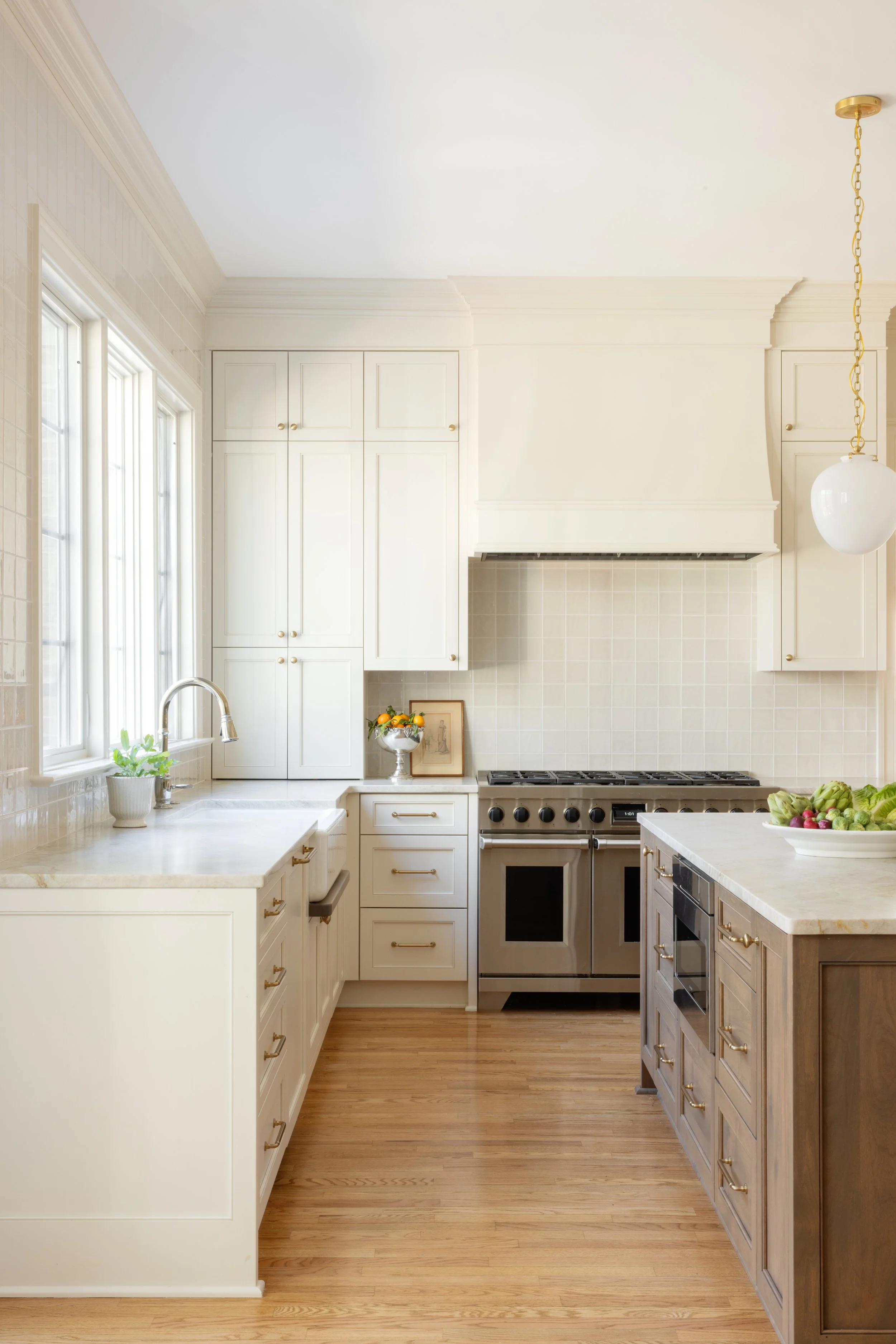 Bright kitchen with white cabinets, marble countertops, wooden floor, stainless steel stove, and a bowl of tomatoes on the island.