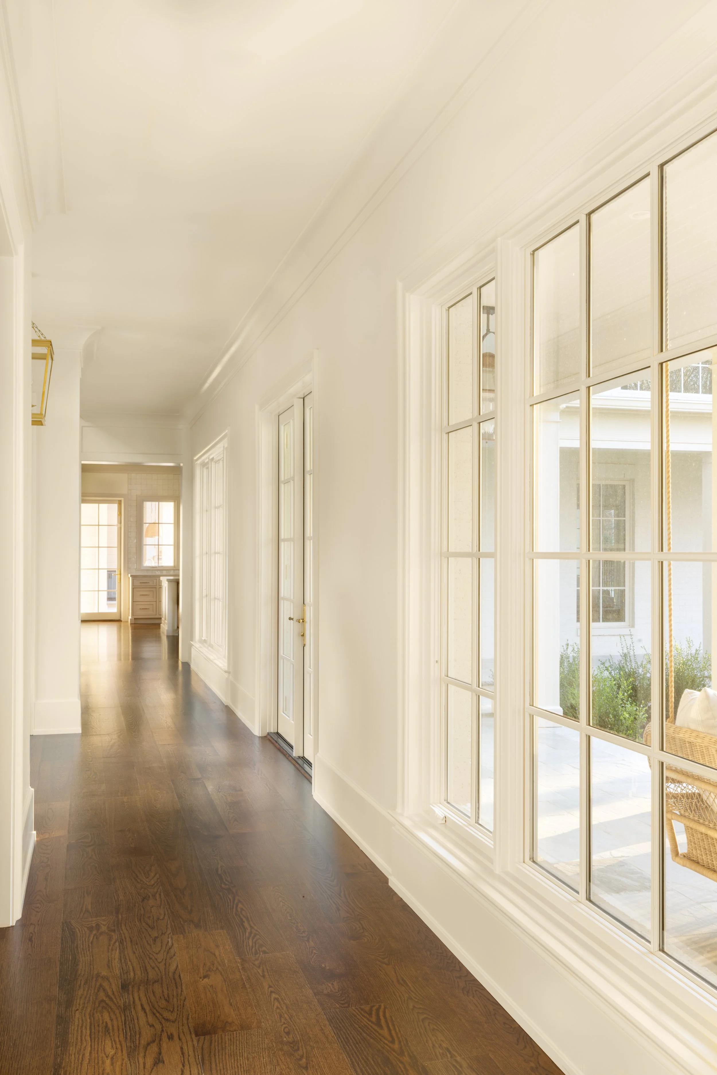 Bright hallway with large windows, white walls, and dark hardwood floors