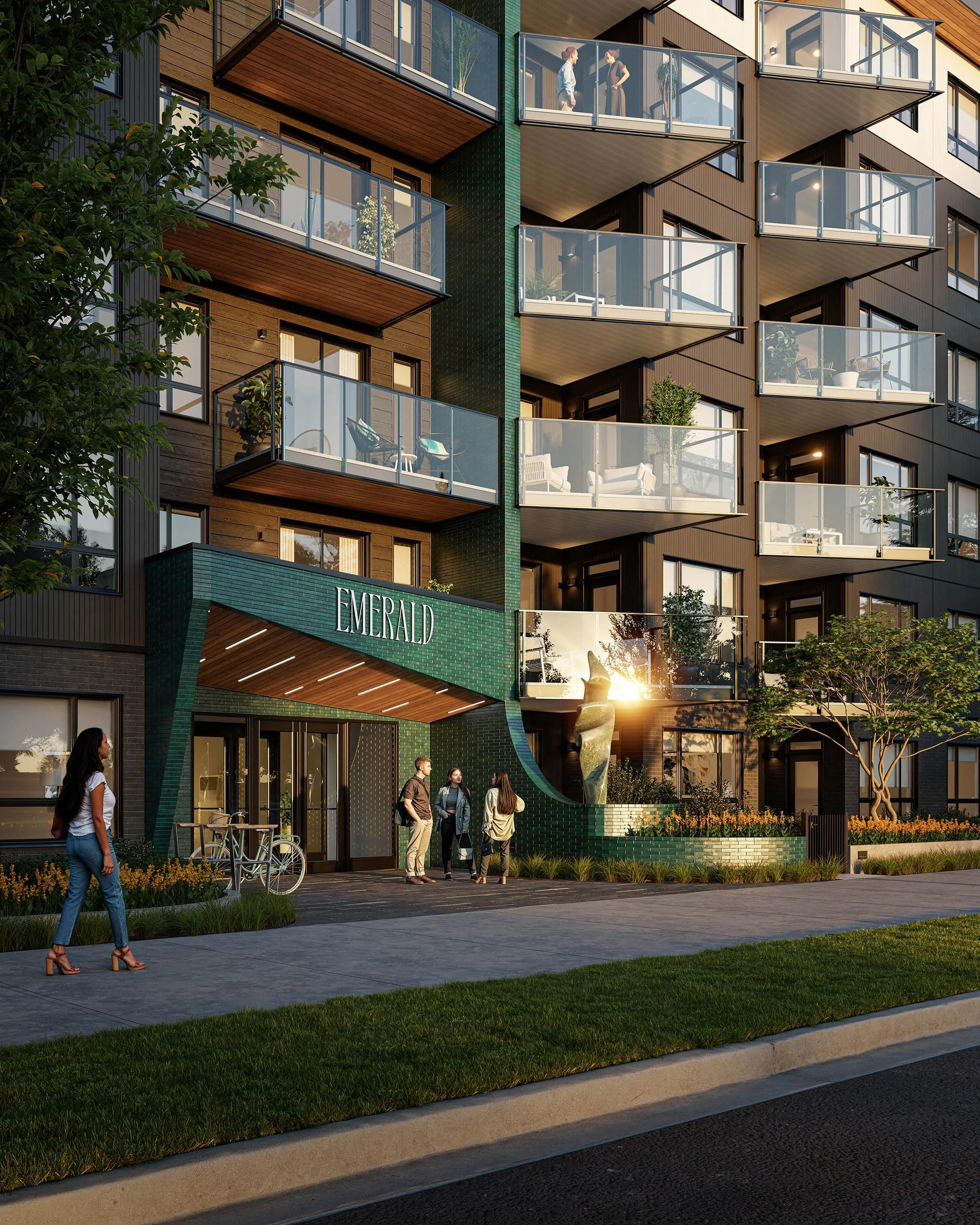 Residential entrance at dusk under a deep green canopy carrying the Emerald name, with a woman walking past on the sidewalk and lit balconies rising above
