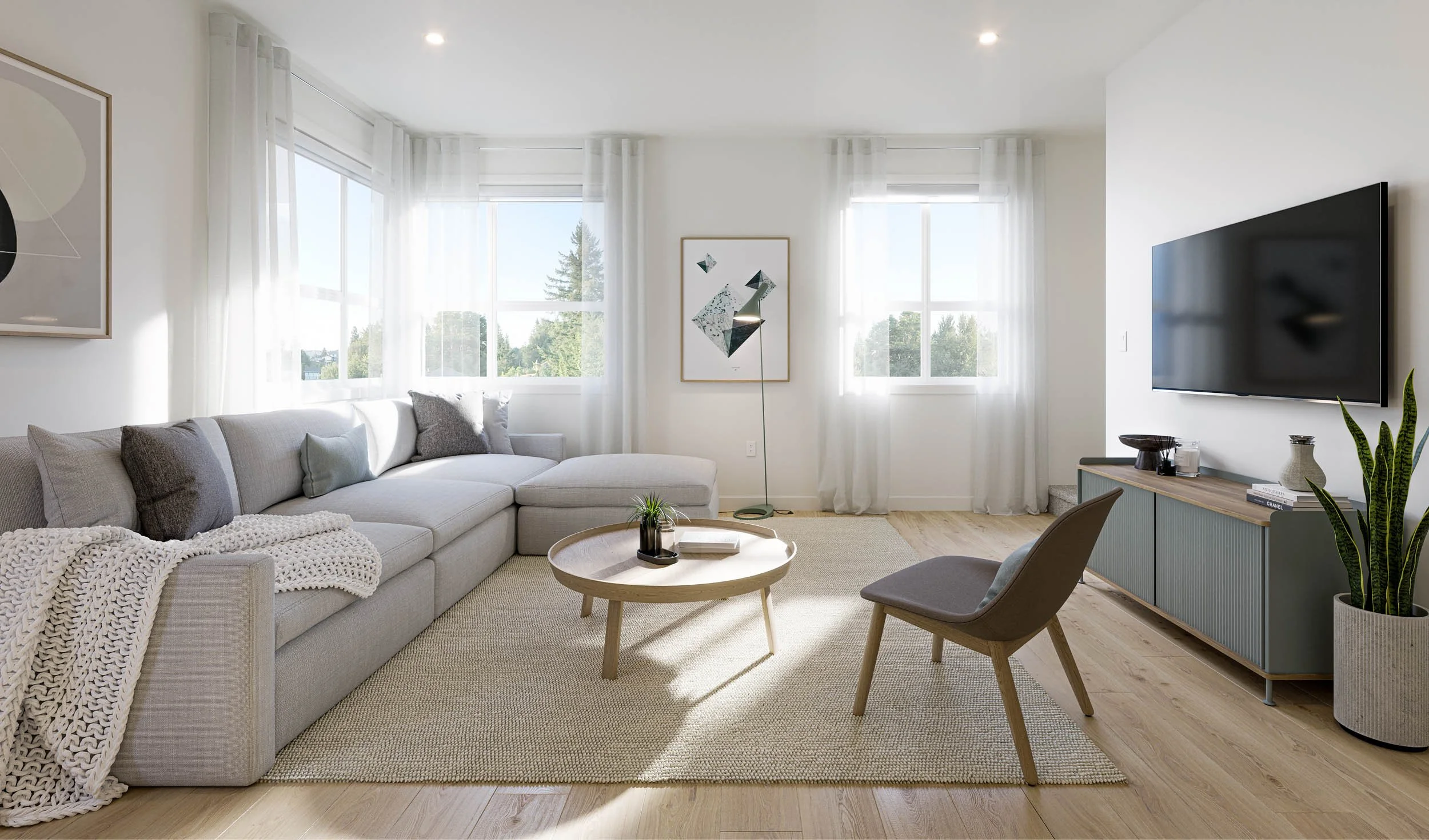 Living room with a pale sectional sofa, round wood coffee table, wall mounted television and two bright windows onto trees