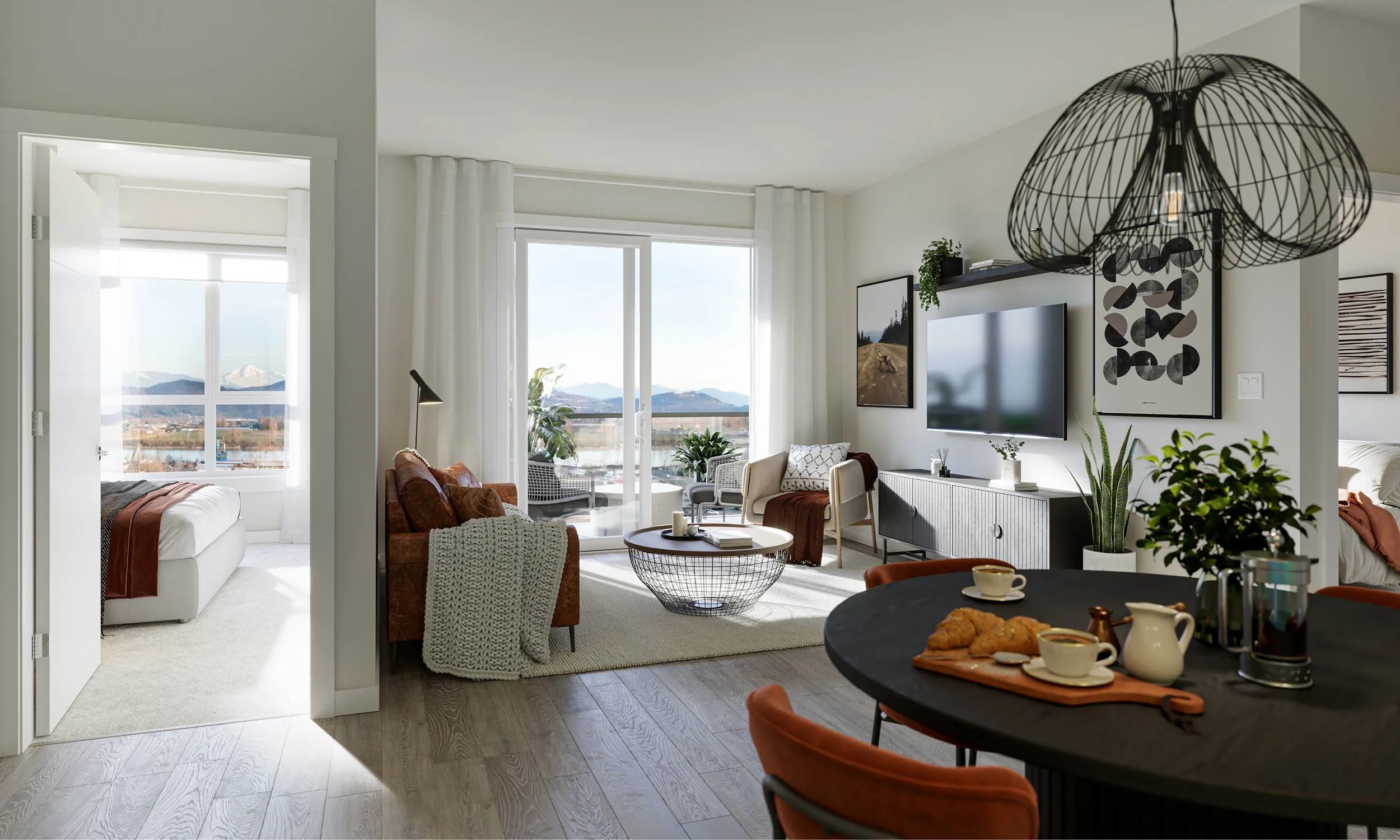 Suite living and dining area with a round dining table set for breakfast, a sofa and television, and a balcony door onto a mountain view