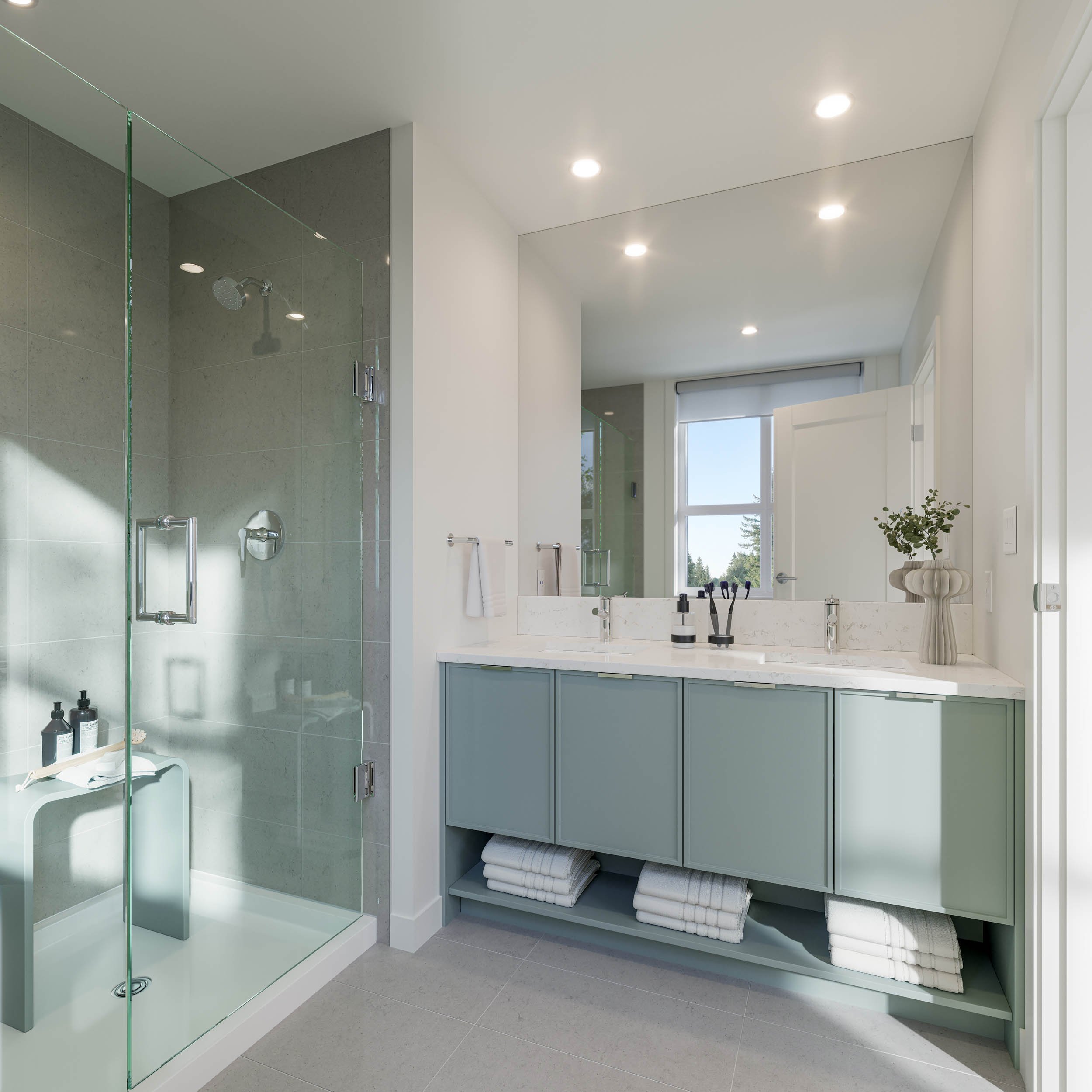 Ensuite with a glass walk in shower, a sage green double vanity, folded towels on an open shelf and a wide mirror above