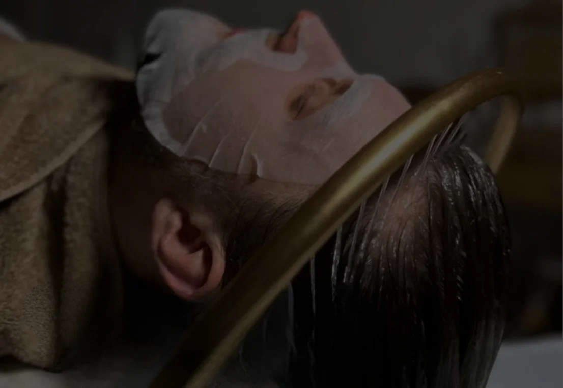 Personne allongée avec un masque facial, des taches blanches, ayant des cheveux foncés, probablement en soin de beauté ou en spa.