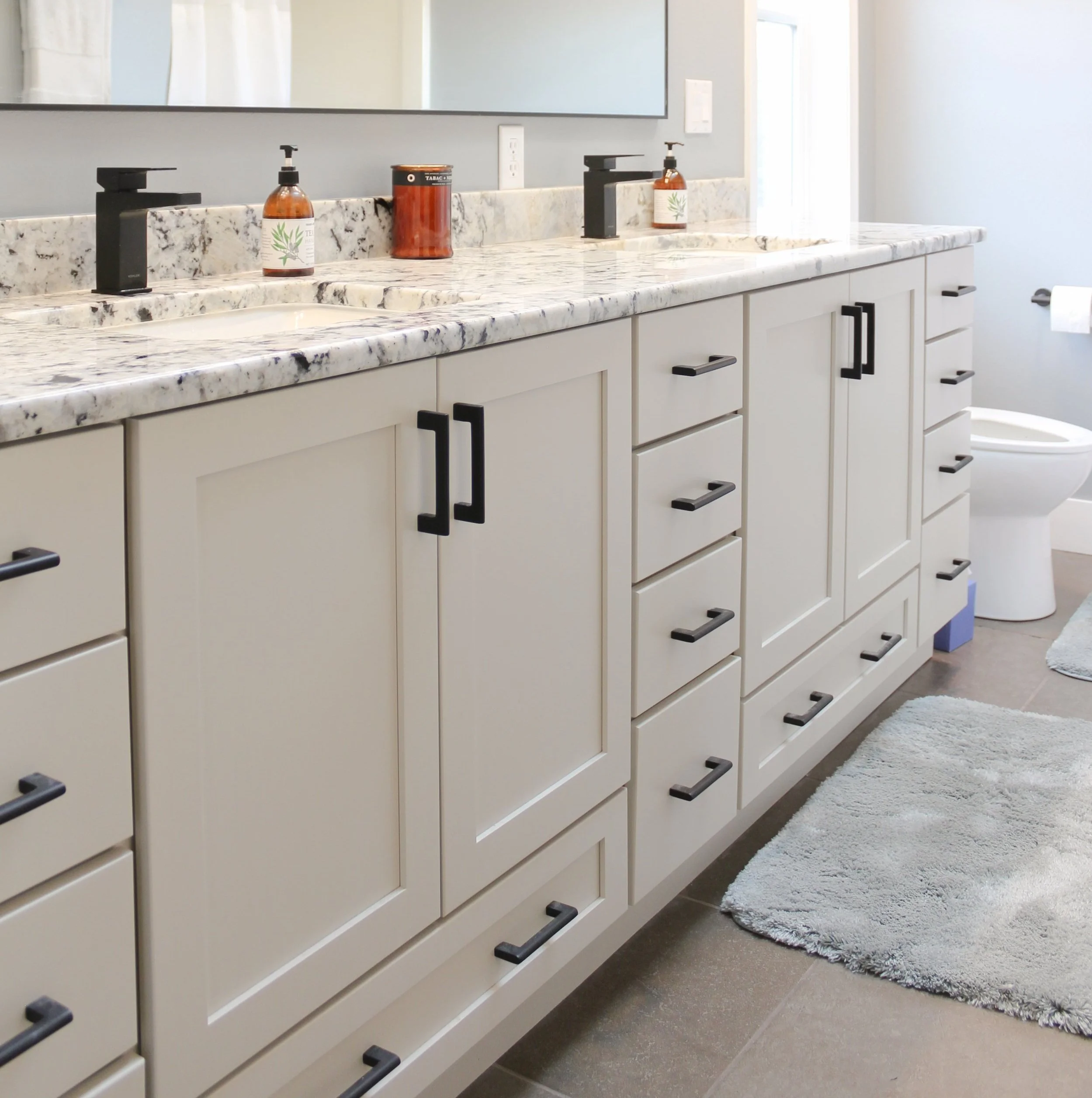 Gray kitchen cabinet with a stainless steel gas cooktop and black knobs set into a white countertop.