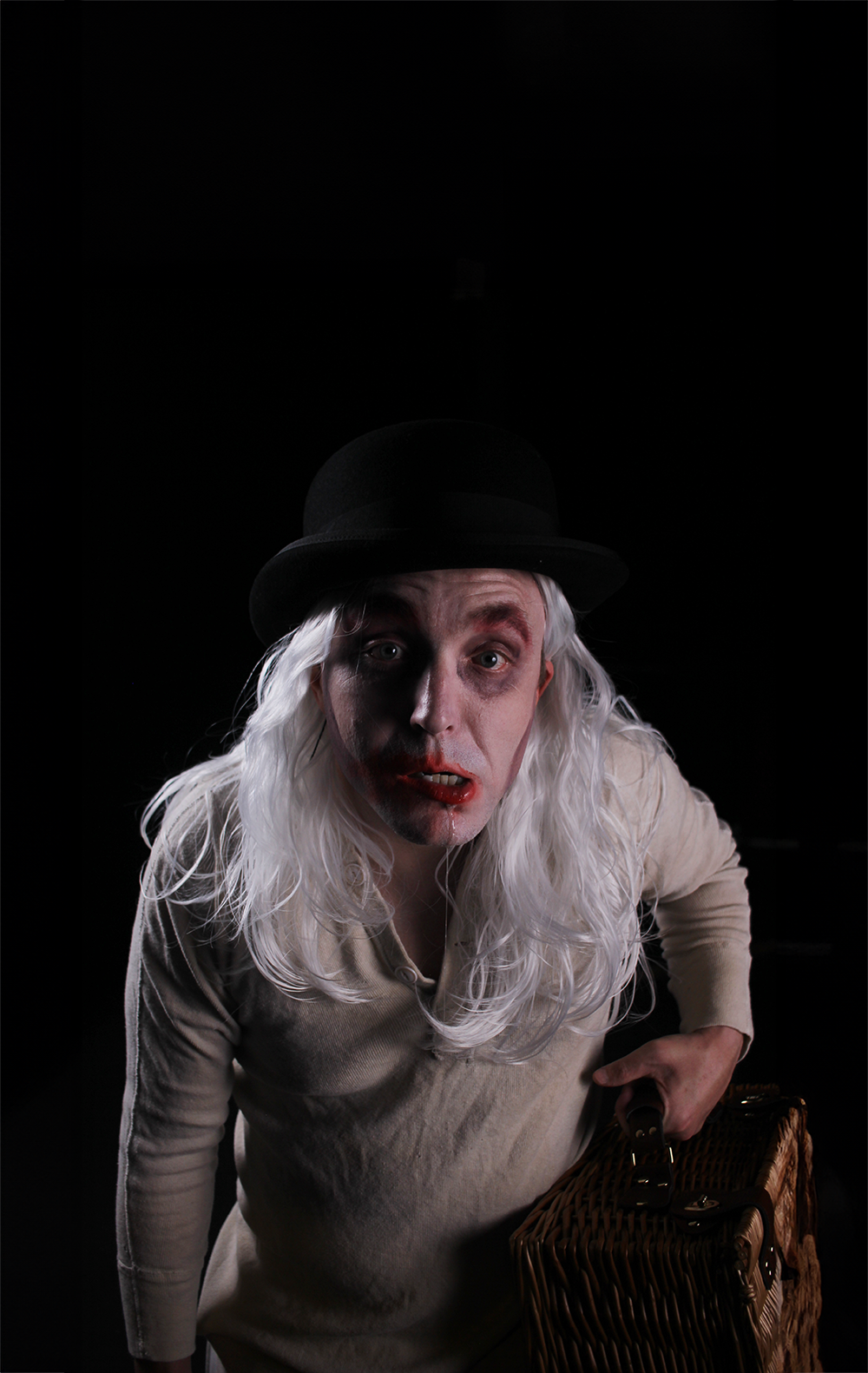 white man with long white hair wearing bowler hat, with hollow eyes and smeared red lips