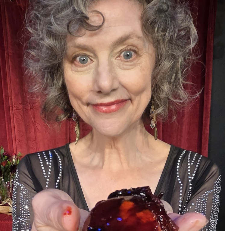 an older white woman with gray curls wearing a black and silver dress, smiles at the camera, offering you her heart