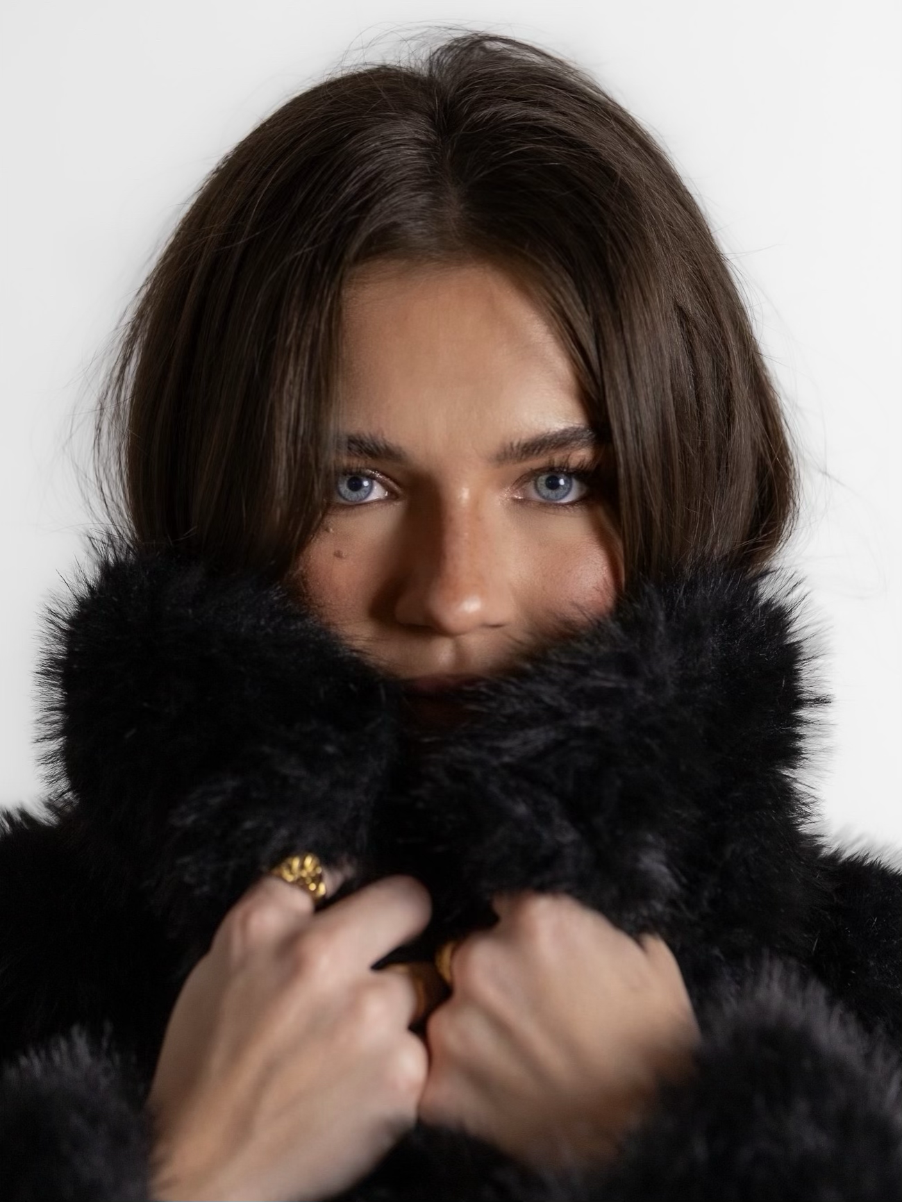A woman with blue eyes and brown hair, partially covered by black fur, looking directly at the camera