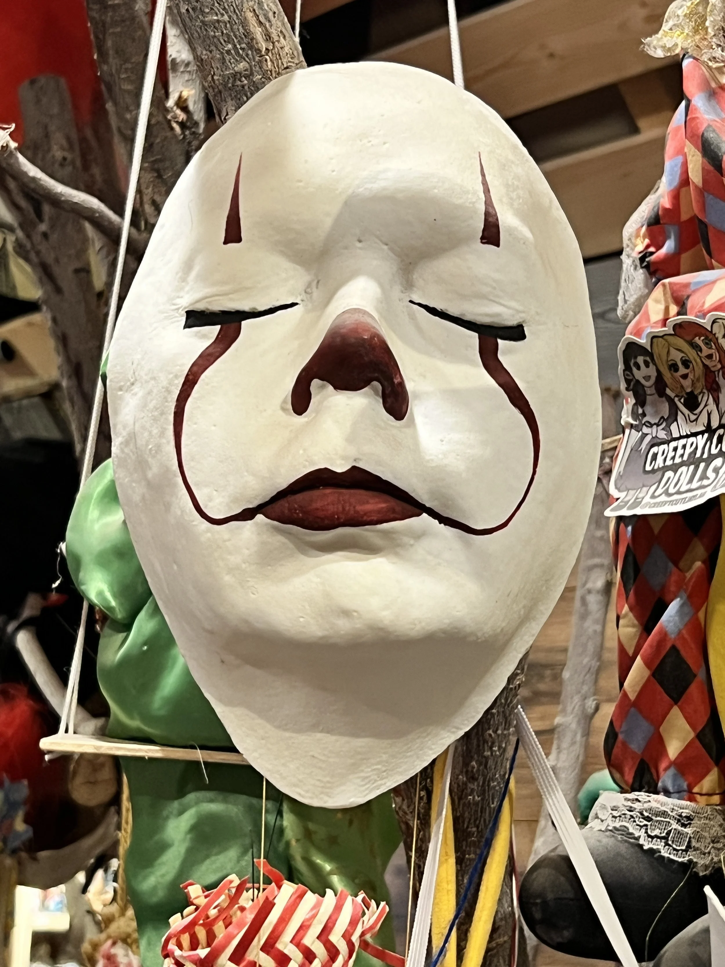 A white theatrical mask with closed eyes and a sad expression, hanging from a display.