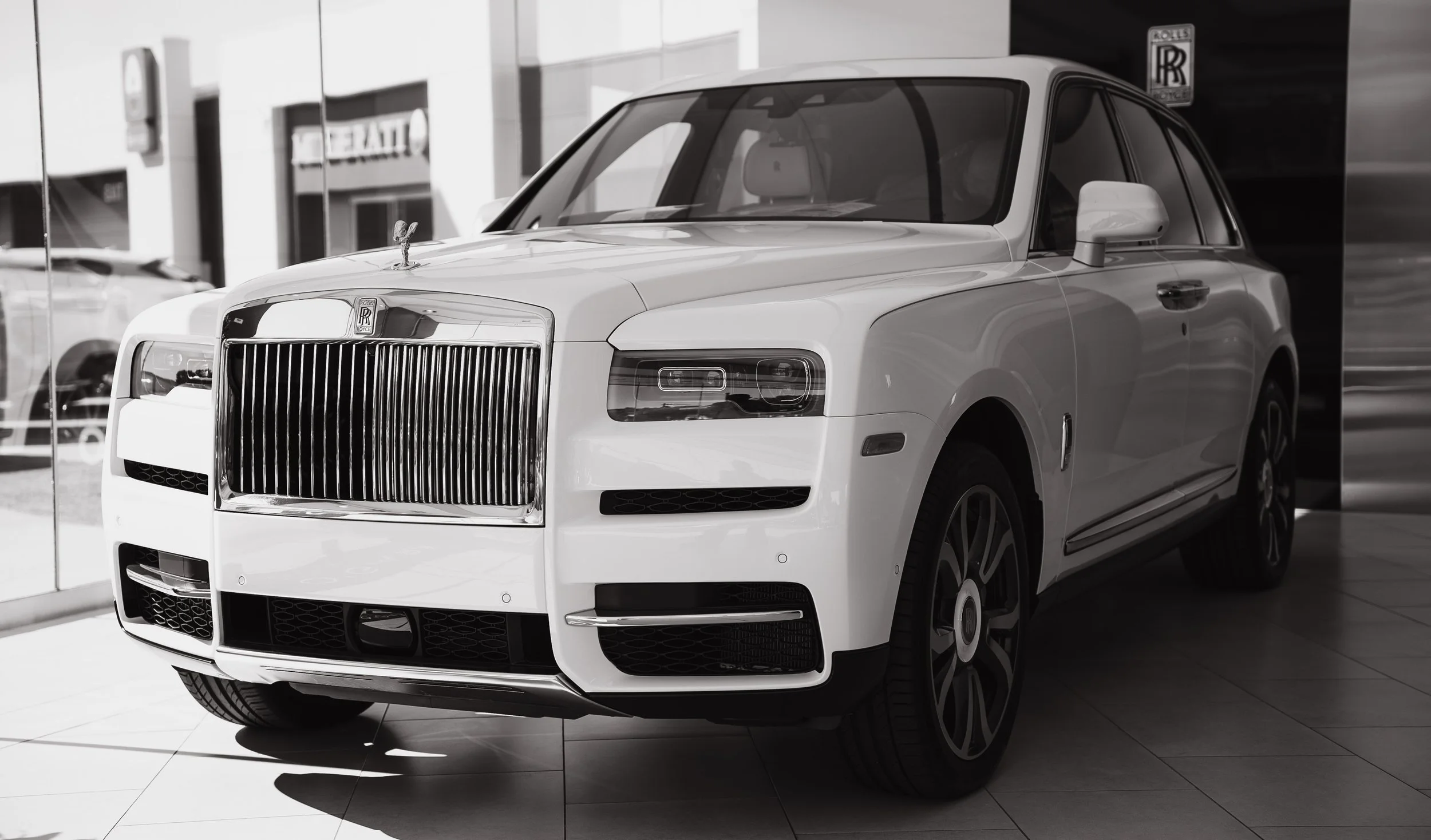 Luxury white Rolls-Royce SUV on display in showroom with reflective glass and Rolls-Royce logo