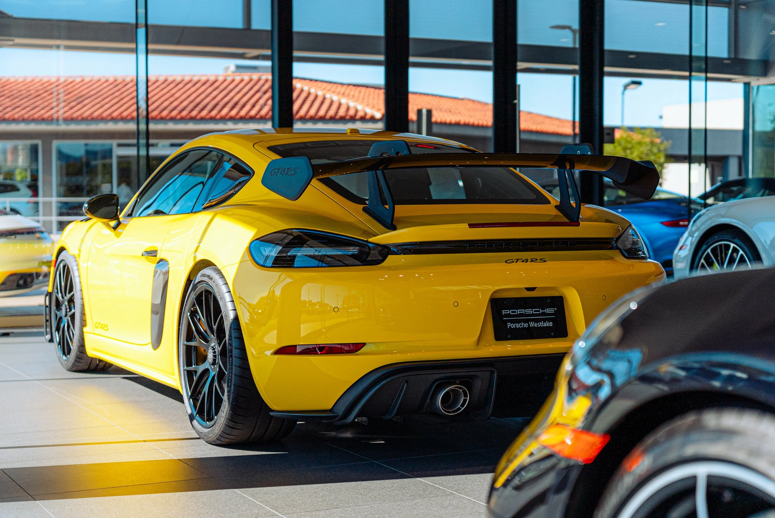 Yellow Porsche sports car with a large rear wing on display inside a car showroom.