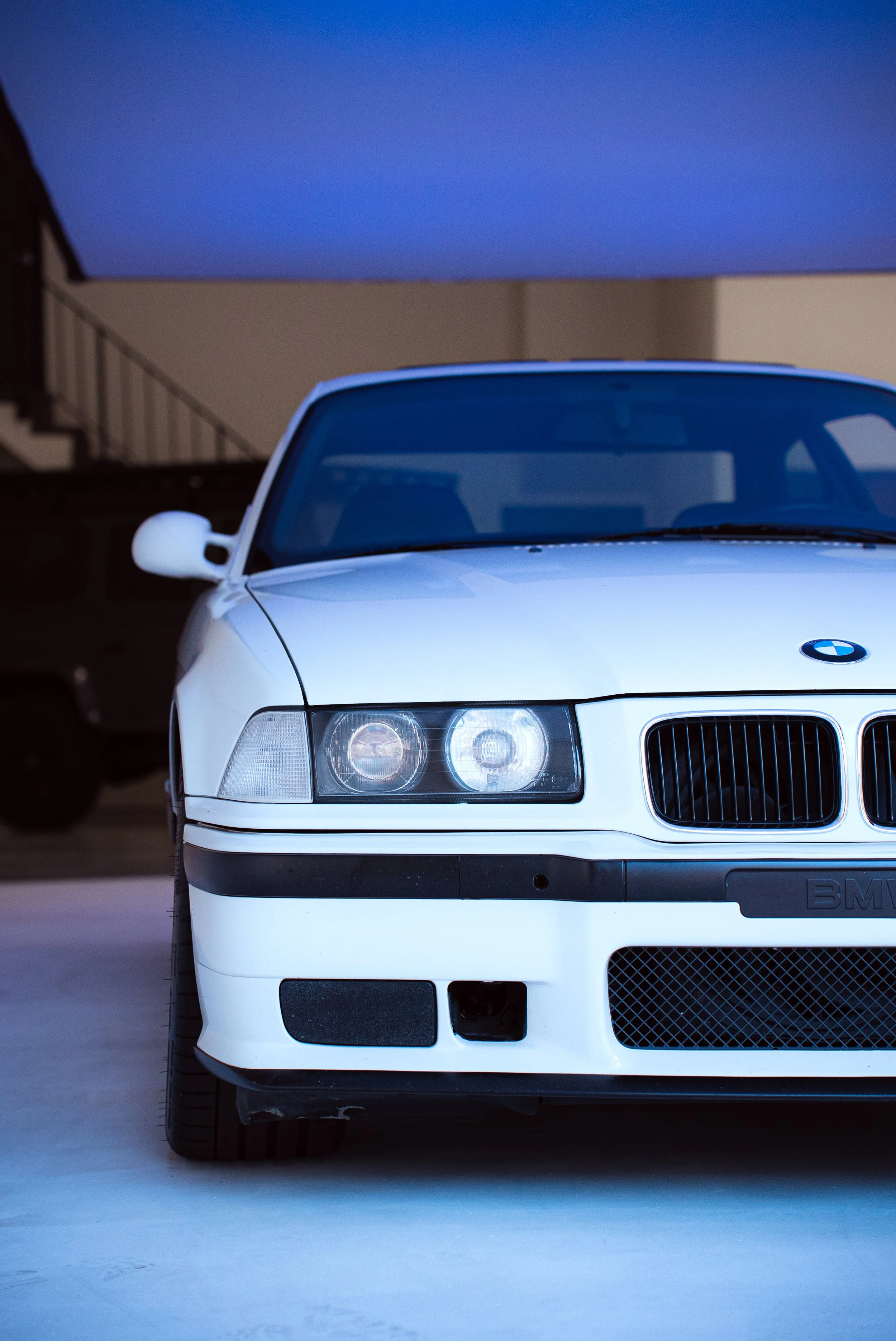 Front view of a white BMW car parked indoors with blue lighting
