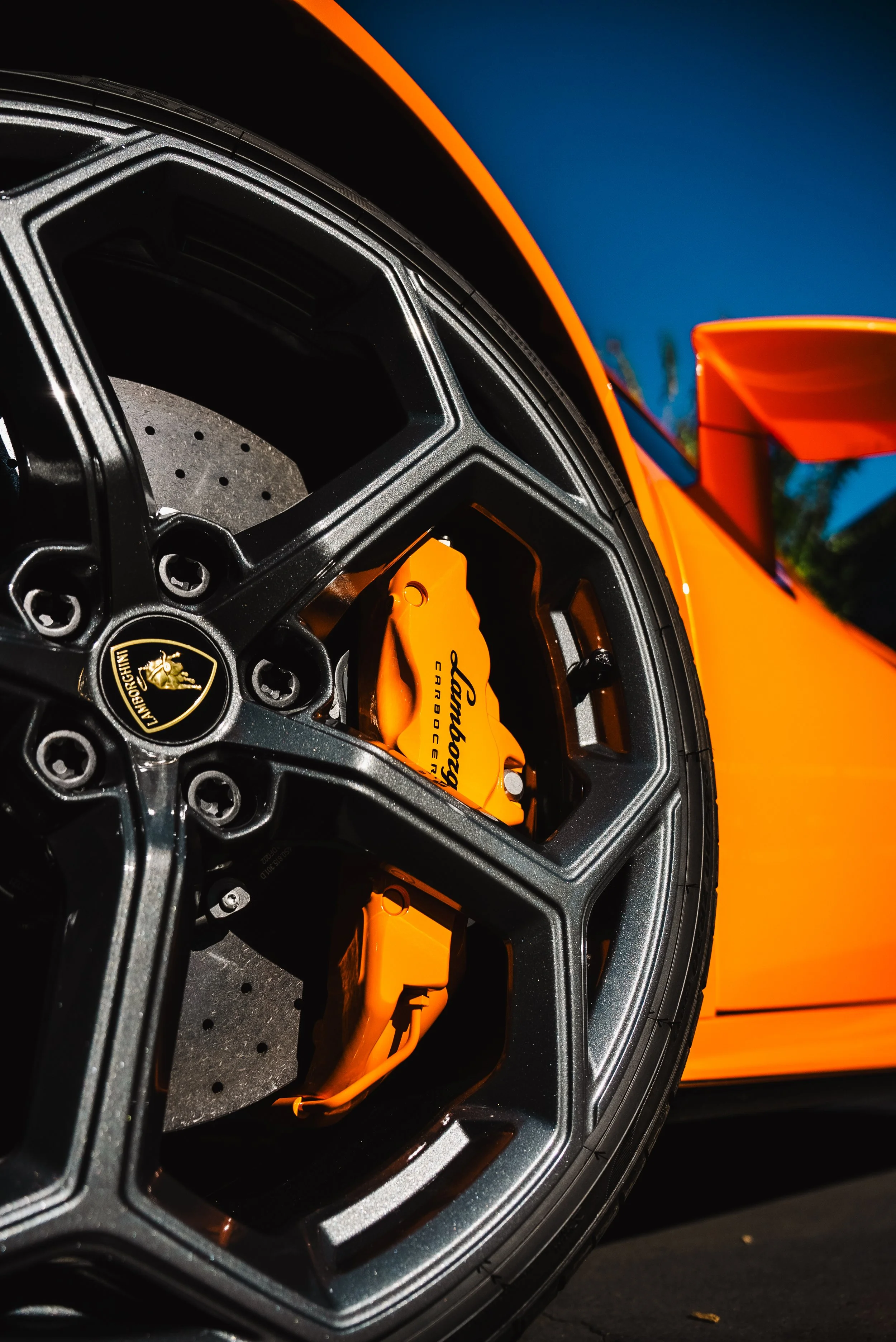 Close-up of a Lamborghini car wheel with a black rim and bright orange brake caliper, part of a vibrant orange sports car.