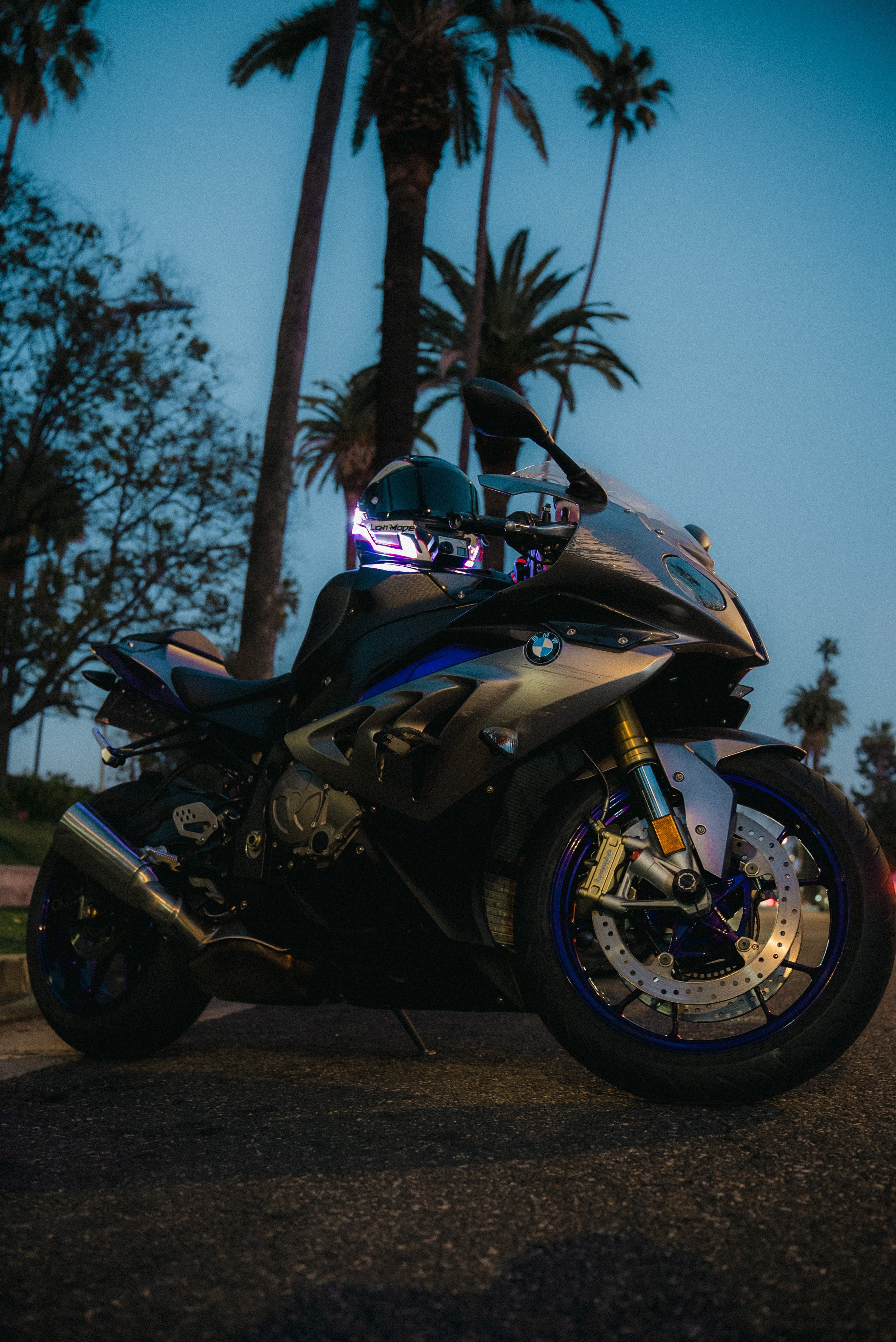 A black and blue BMW sport motorcycle parked on a street with palm trees in the background during dusk.