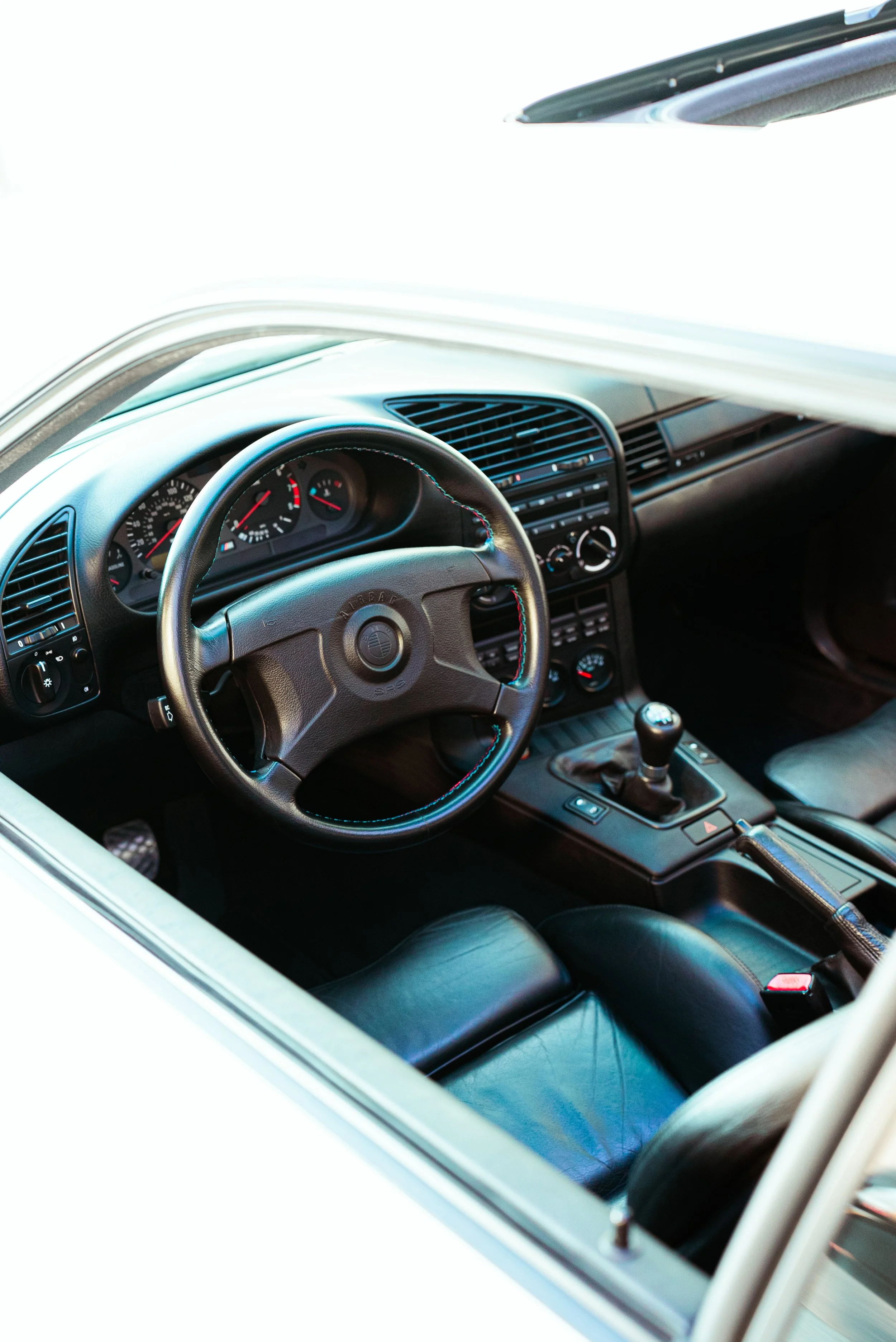 Interior of a classic car showing the steering wheel, dashboard, gear shift, and leather seats.