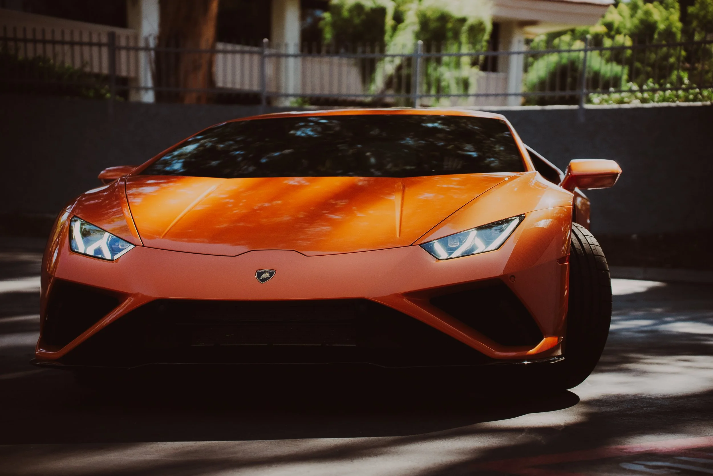 Orange Lamborghini sports car parked outdoors with trees and houses in the background.