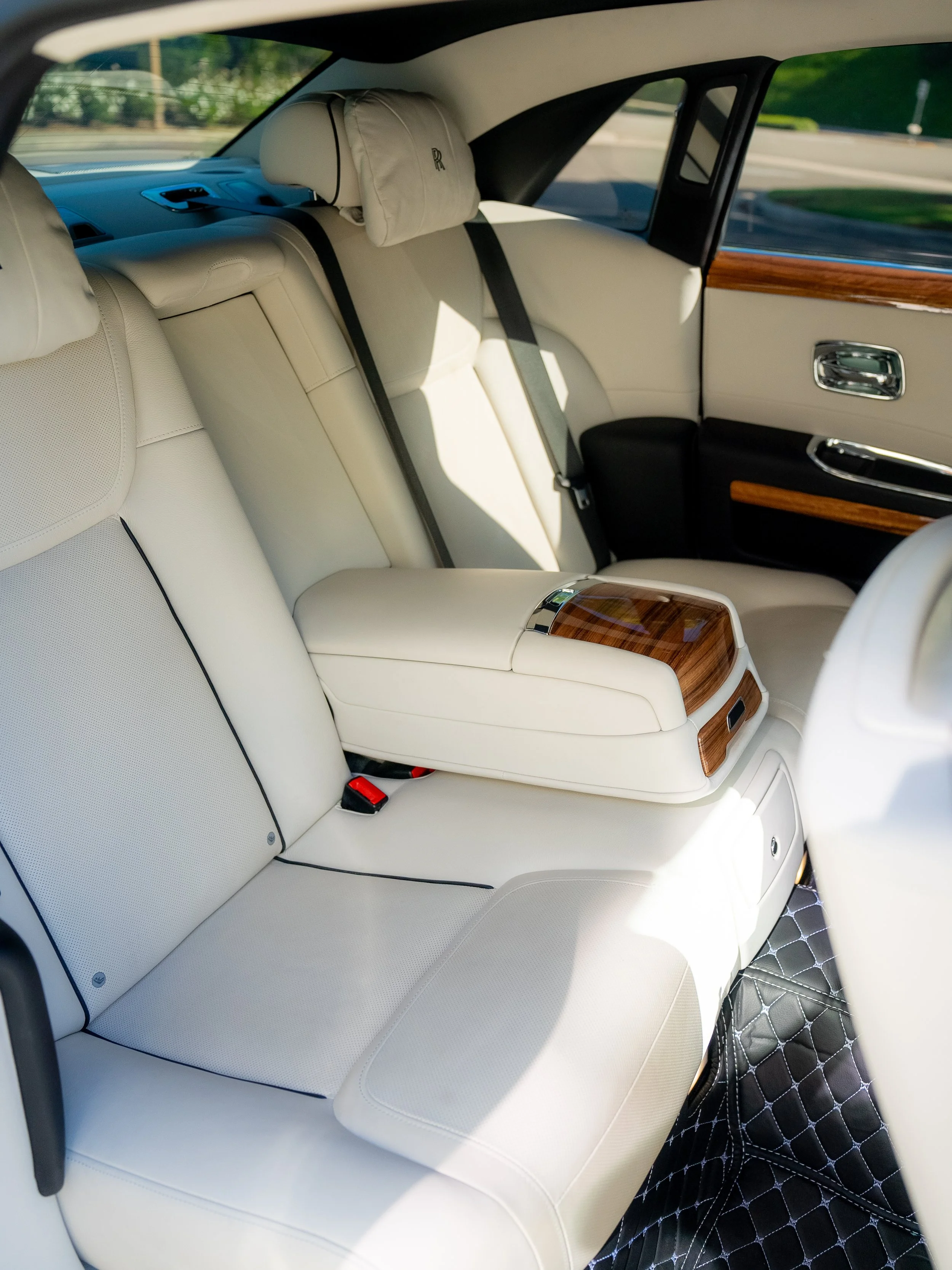 Interior of a luxury car showing cream-colored leather seats, wood trim, and a black quilted floor mat.