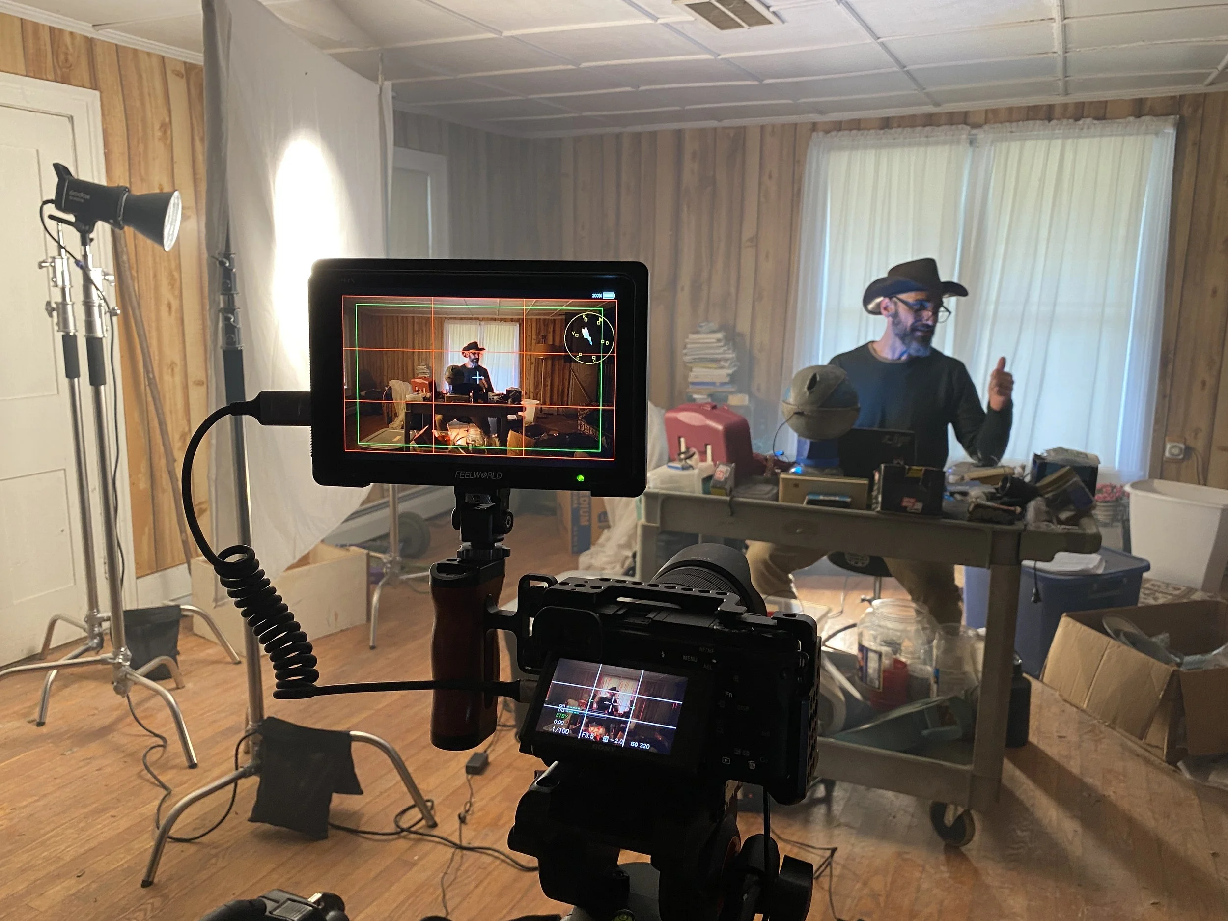 A film set with a camera in the foreground and an actor rehearsing lines in the background