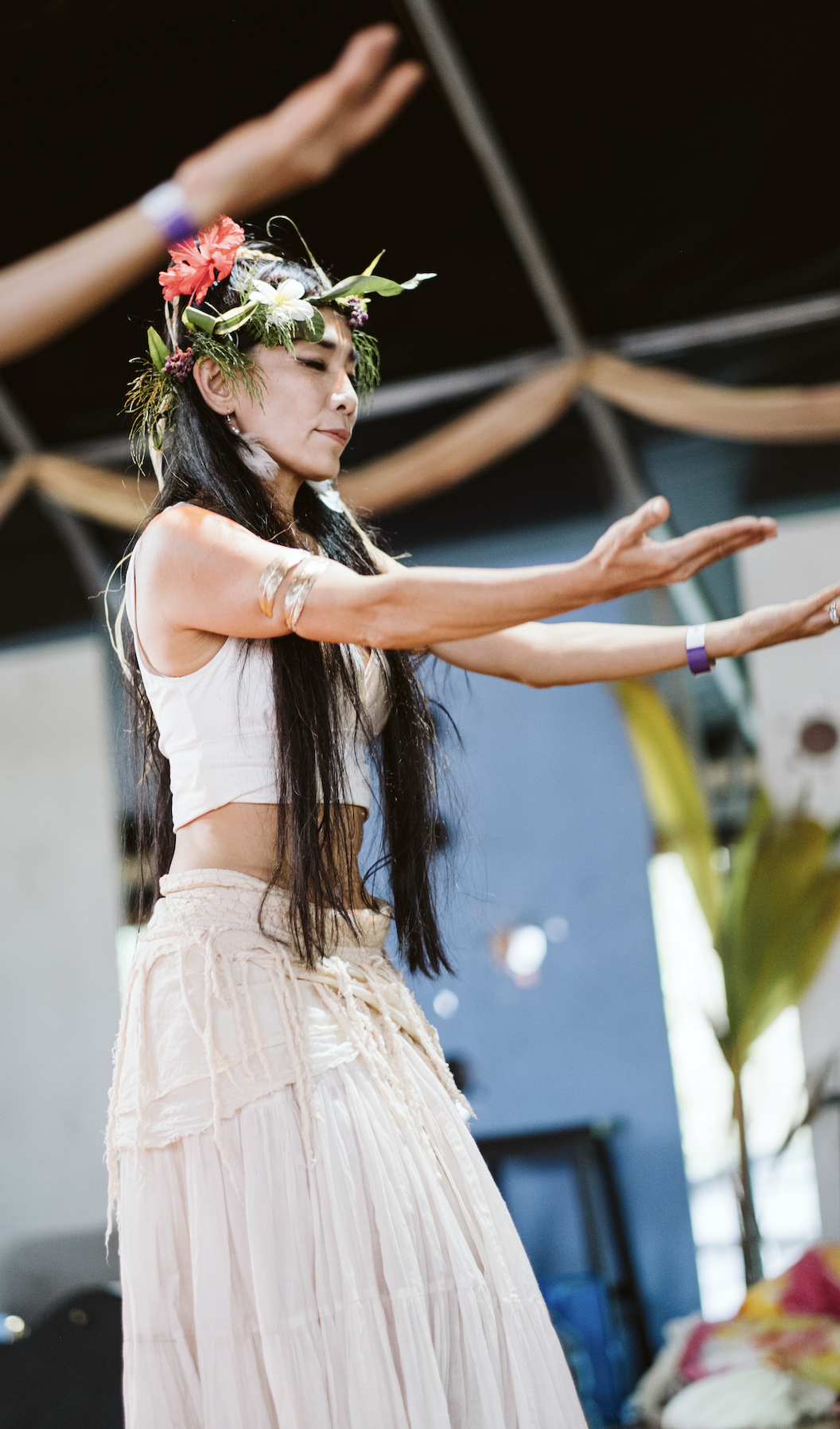 A woman dressed in a white crop top and white skirt, wearing a floral crown, is perfomring Hula at  ManaFest, a transformational music, dance, arts, and culture festival on Big Island of Hawaii 