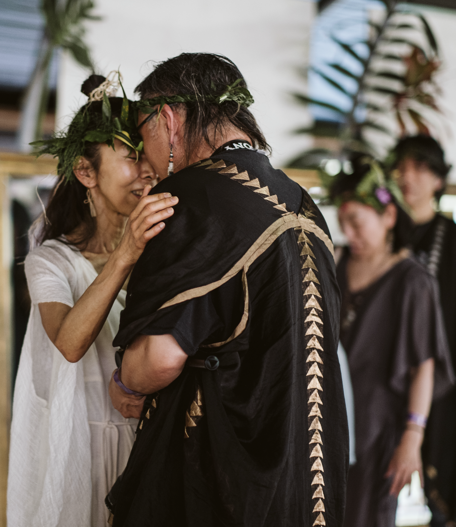 Two Japanese people wearing leaf crowns sharing an emotional moment, with other women wearing leaf crowns at  ManaFest, a transformational music, dance, arts, and culture festival on Big Island of Hawaii 