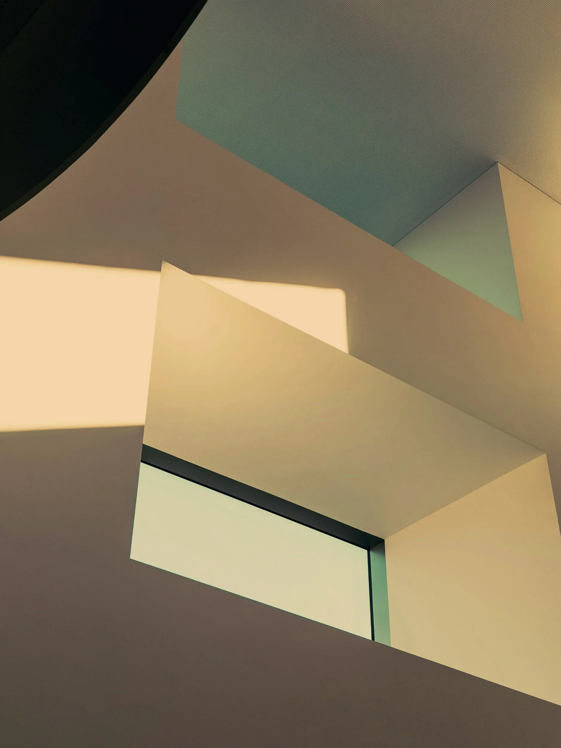 Ceiling view of modern architecture with angular, geometric shapes and soft lighting, emphasizing clean lines and subdued colors.