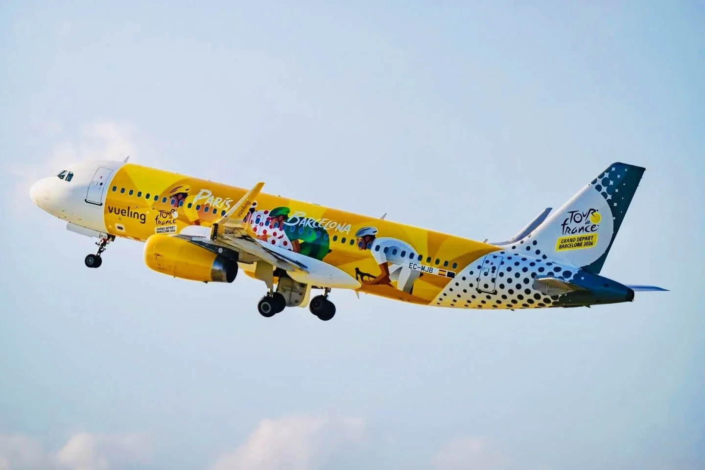 Commercial airplane decorated with sports-themed artwork, promoting the Tour de France 2026, with illustrations of cyclists and city names like Paris and Barcelona on a clear sky background.