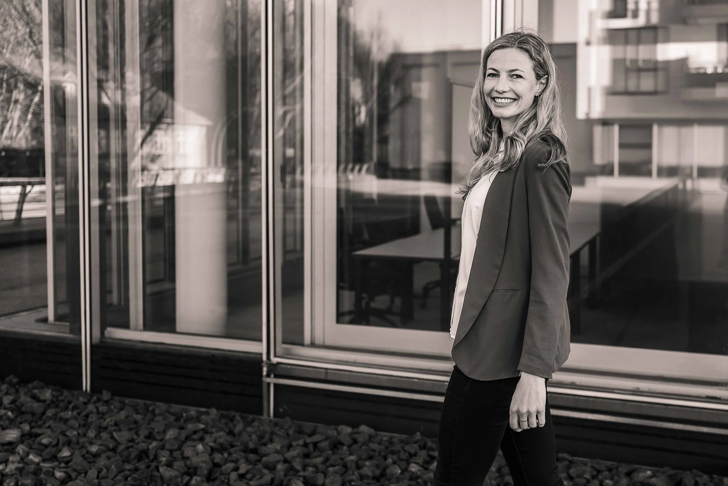 Sympathisches schwarz-weißes Business Portrait einer Frau in Hamburg, freundlich lächelnd vor hellem Hintergrund.