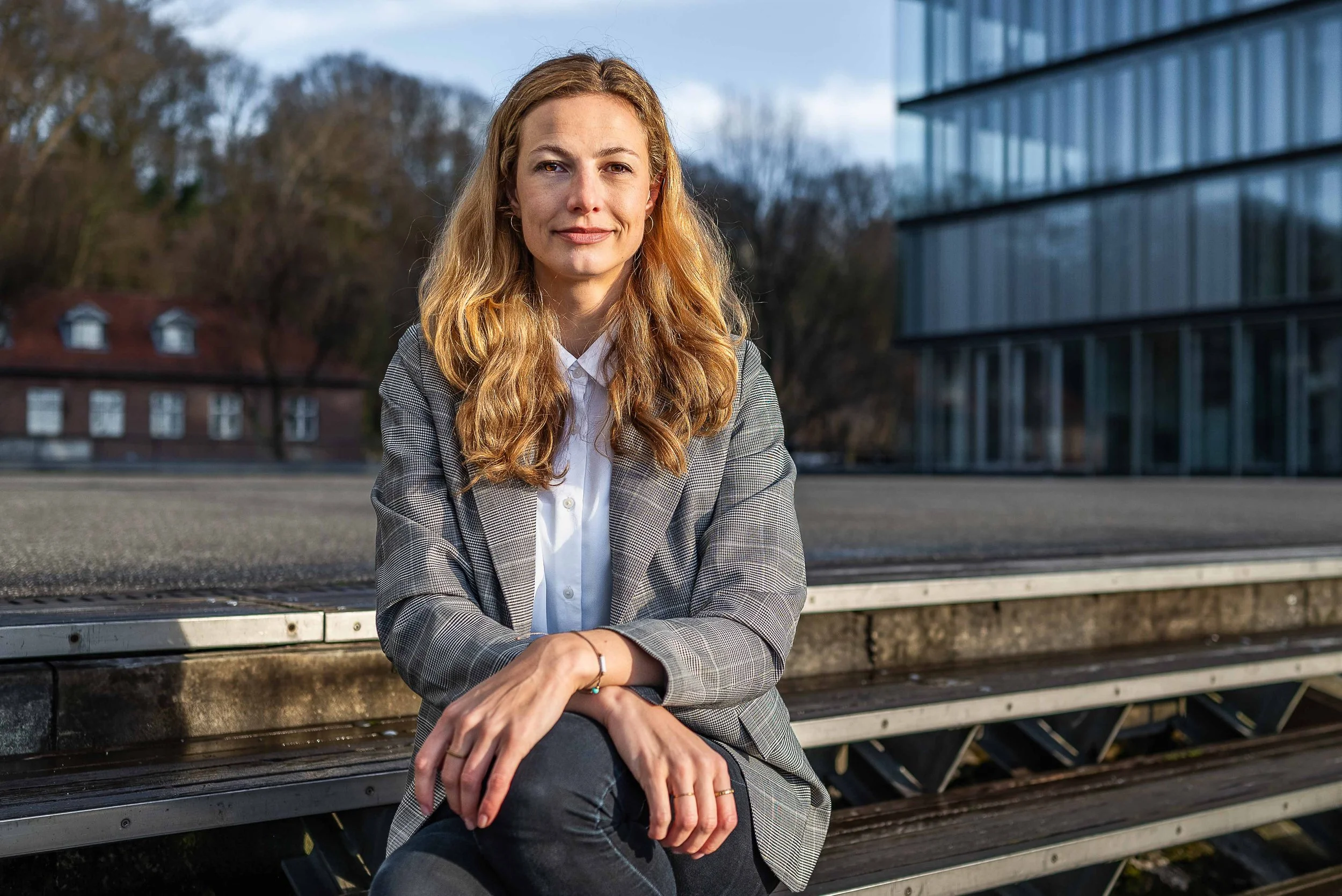 Ausdrucksstarkes Business Portrait einer blonden Frau im Blazer in Hamburg, sehr freundlich lächelnd vor urbanem Hintergrund.