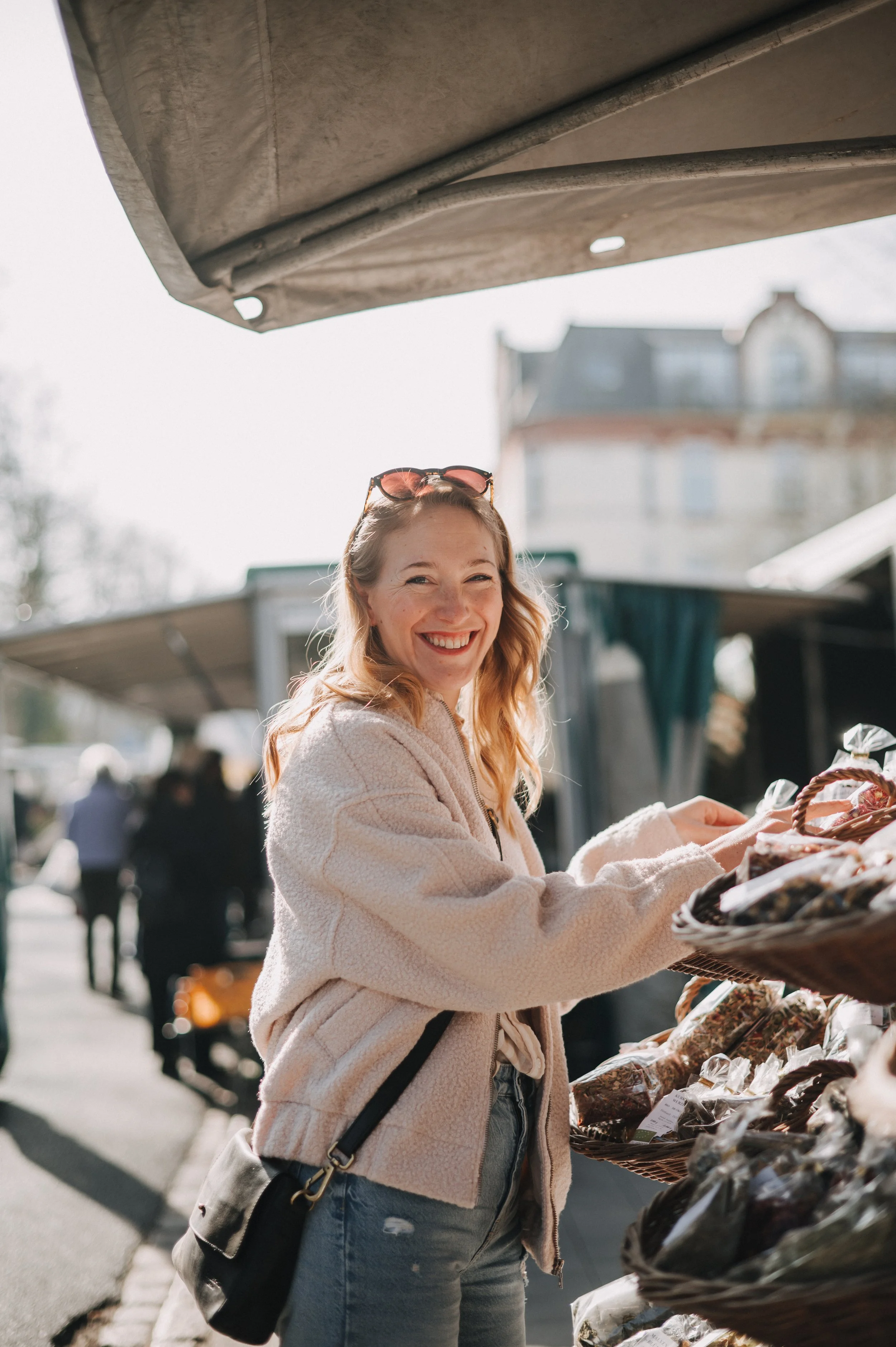 Lächelnde Frau beim Einkaufen auf einem Markt, umgeben von Obst und Gemüse.