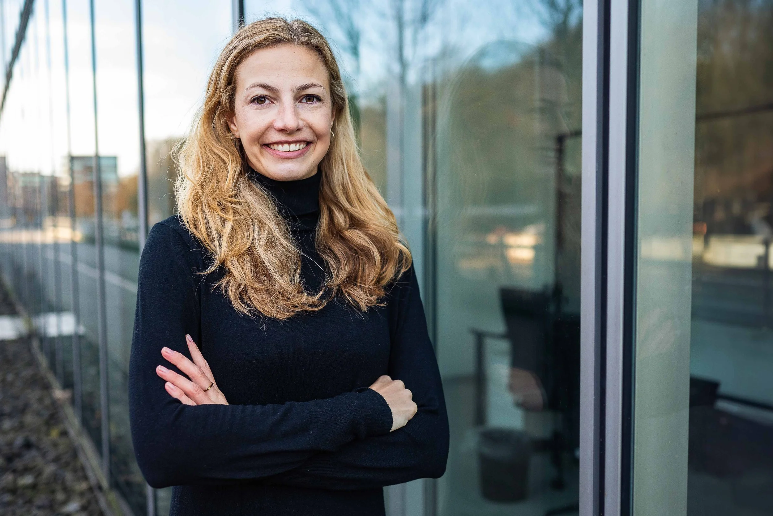 Sympathisches Business Portrait einer Frau im schwarzen Pullover in Hamburg, natürlich lächelnd vor hellem Hintergrund.