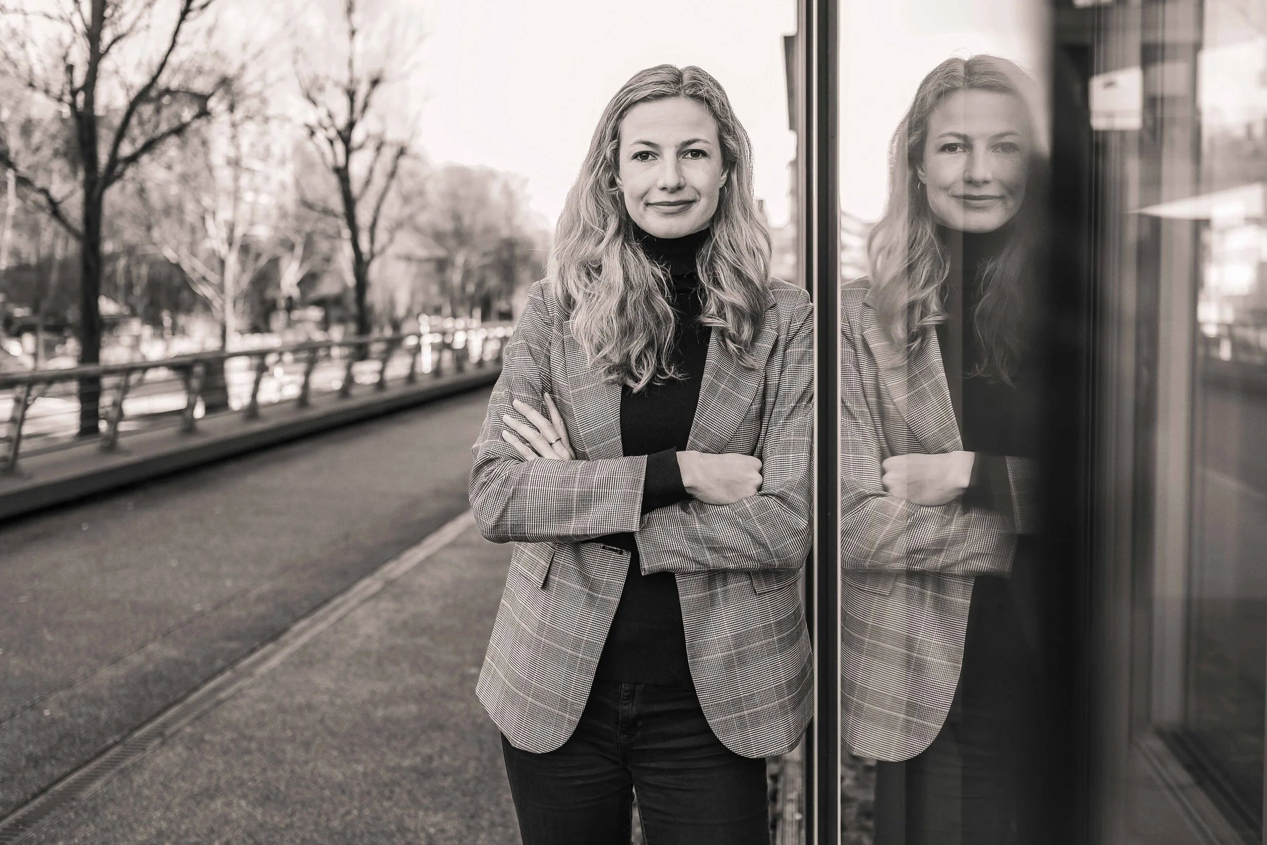 Sympathisches schwarz-weiß Business Portrait einer blonden Frau im Blazer in Hamburg, sehr freundlich lächelnd vor urbanem Hintergrund.