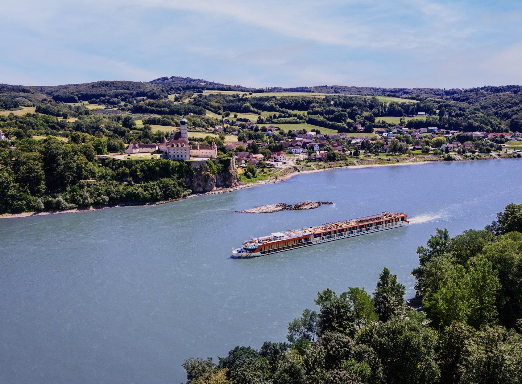 A scenic river scene with a long passenger cruise boat moving through calm waters near a lush green town and rolling hills.