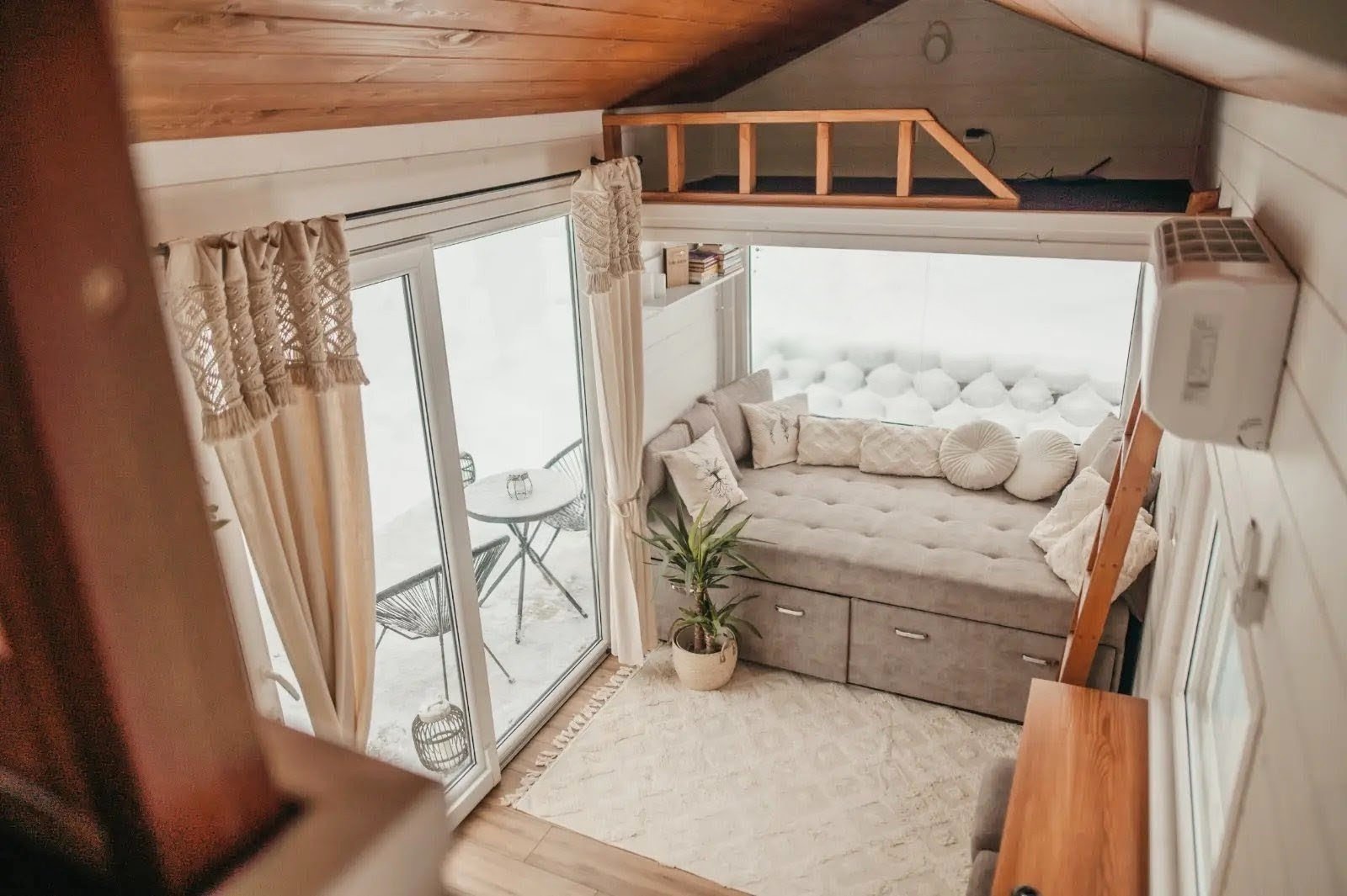 Gemütliche Hütte mit Alkoven, Polstermöbeln, Balkon mit Sitzbereich, Pflanzen und Vorhängen.