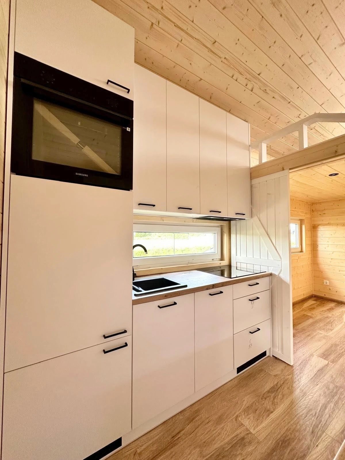 Küchenbereich mit weißen Schränken, Holzarbeitsplatte, Spüle, kleiner Fenster und Holzdecke in einem Raum mit Holz wänden und Boden.