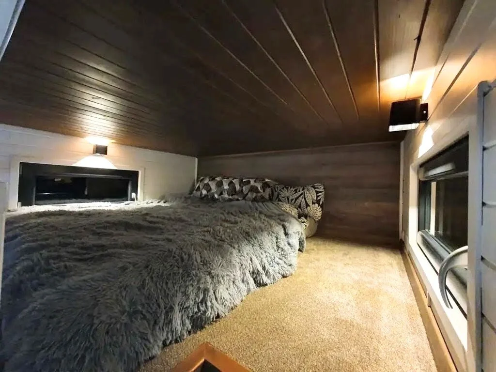 Ein gemütliches Schlafzimmer mit einer großen, kuscheligen Bettdecke, Kissen mit Mustern und kleinen Wandlampen im Dachgeschoss.