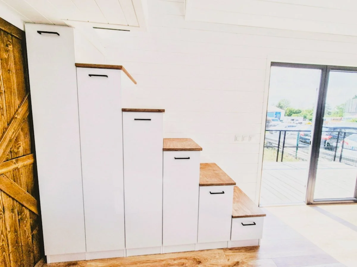 Modulare Treppen aus weißen Schränken mit Holztresen in einem modernen Raum mit großen Fenstern und Holzfußboden.